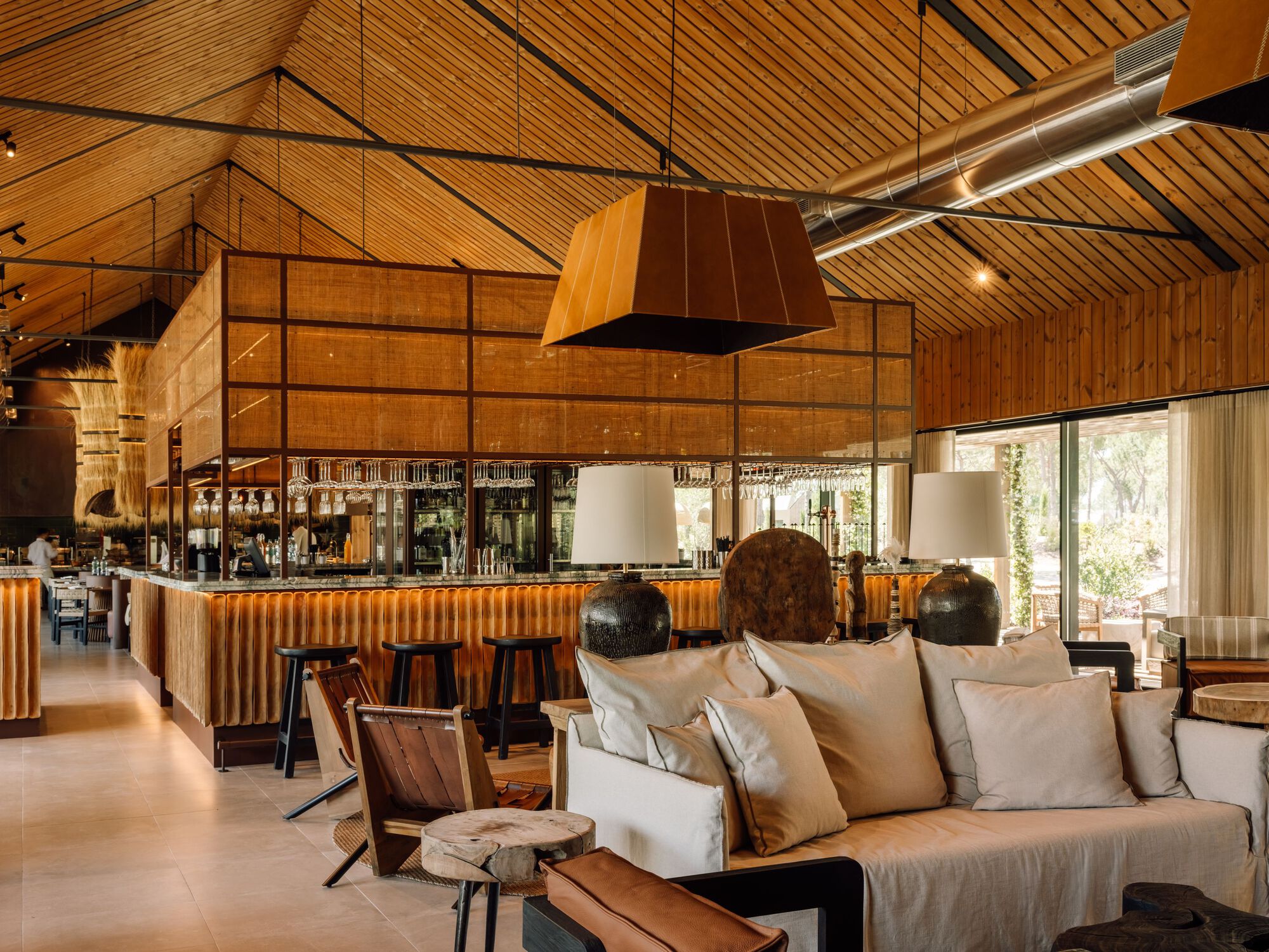 Lounge area with timber-lined vaulted ceiling, corrugated metal bar front and copper pendant lights