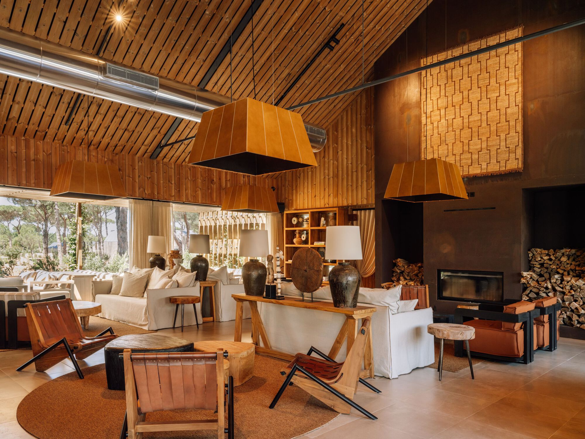 Interior view showing fireplace with stacked firewood, timber ceiling and angular copper pendant fixtures