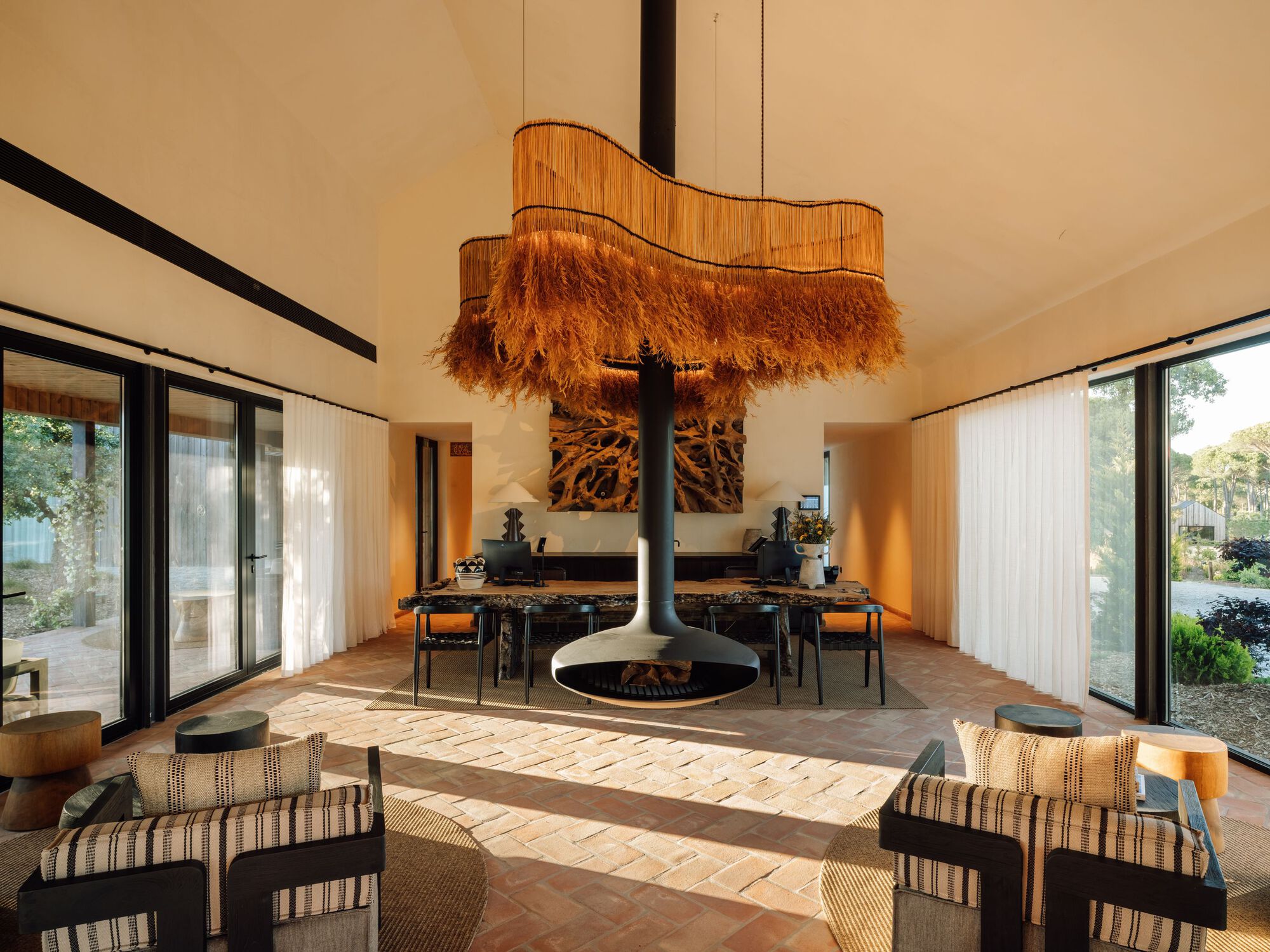Dining space with central suspended fireplace, fringed timber chandelier and glass doors to courtyard