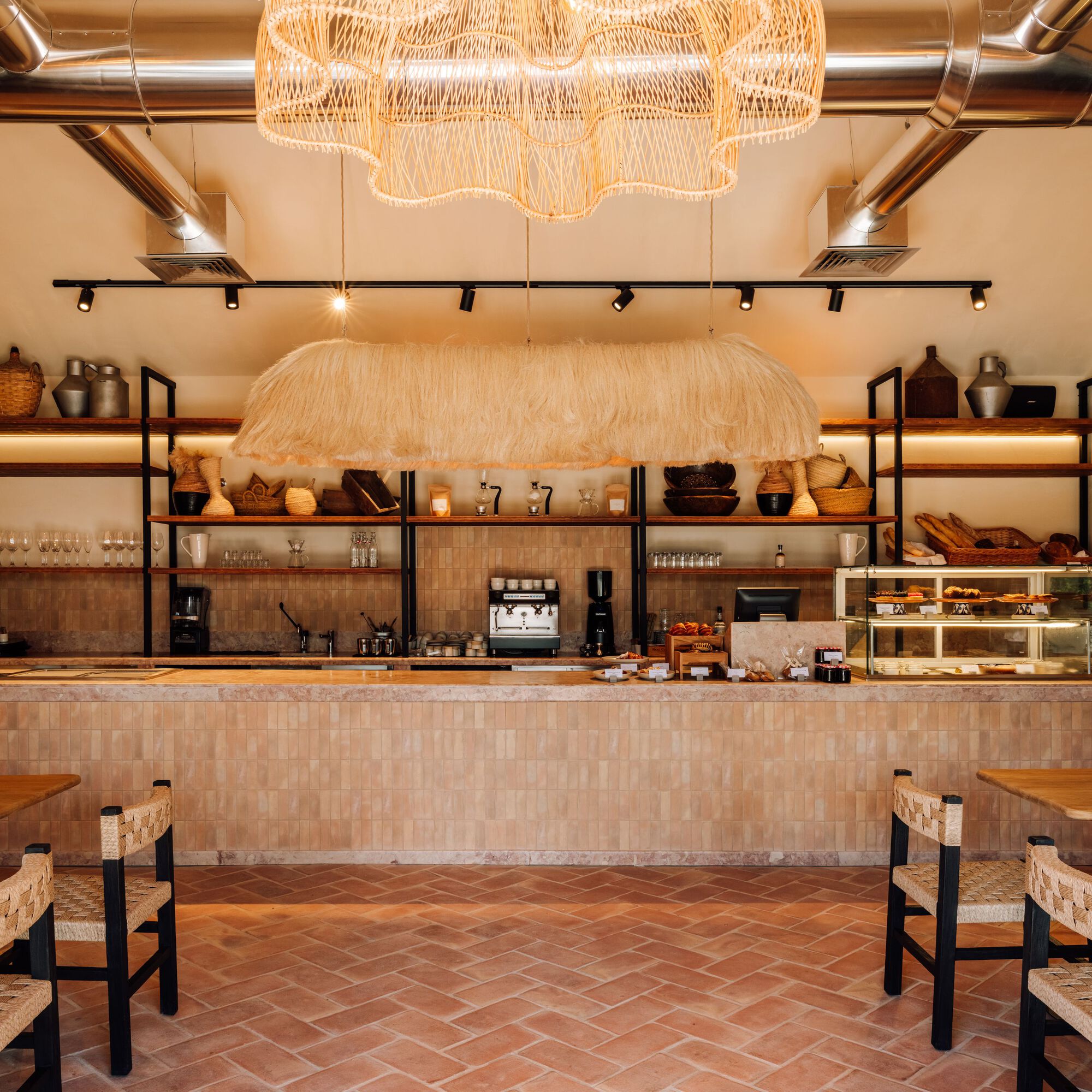 Service counter with mosaic tile front, woven pendant lights and open shelving displaying ceramics