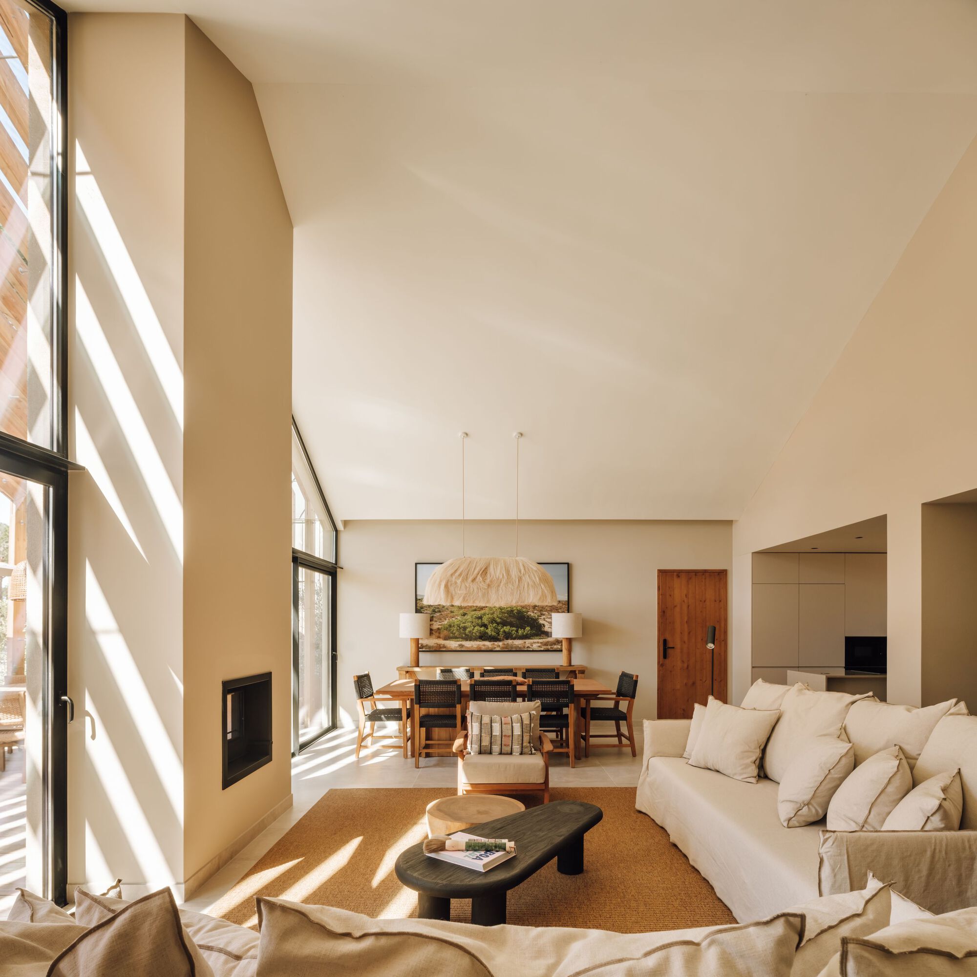 Double-height living space with slanted ceiling and floor-to-ceiling windows casting morning shadows across the floor