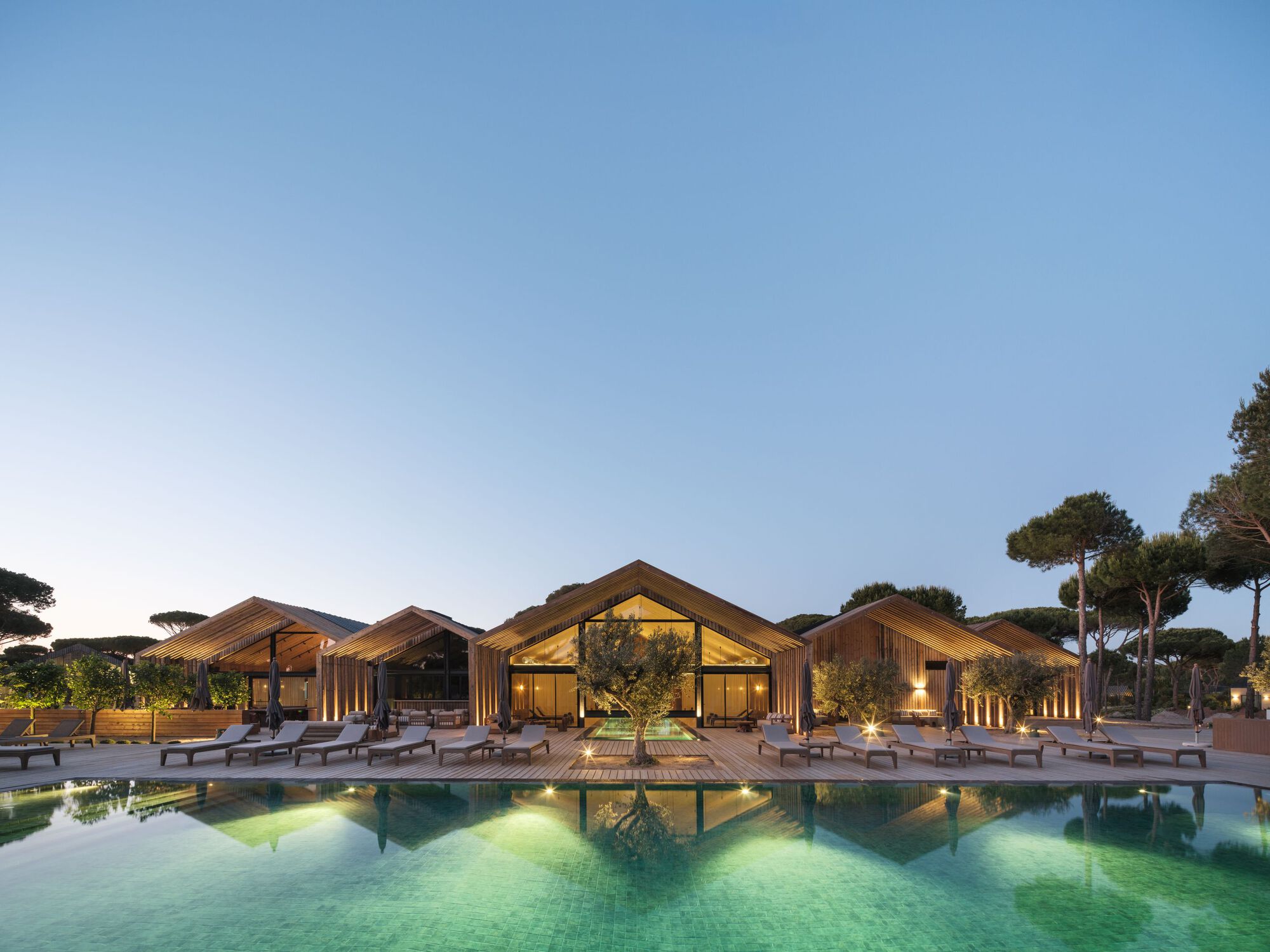 Poolside view of the gabled timber pavilions with exposed rafters under an evening sky