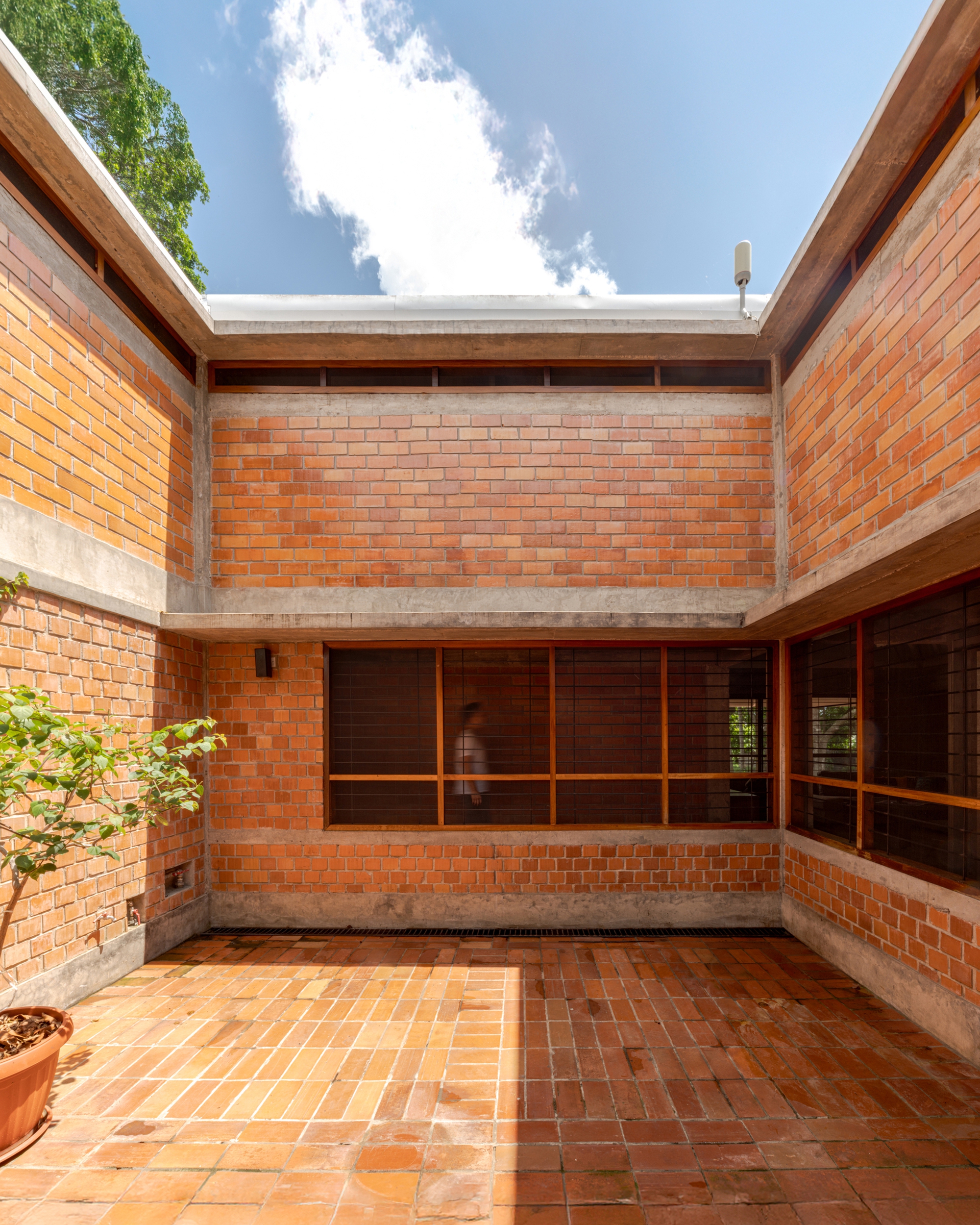 Interior courtyard with terracotta brick paving and walls surrounding timber-framed glazing under open sky