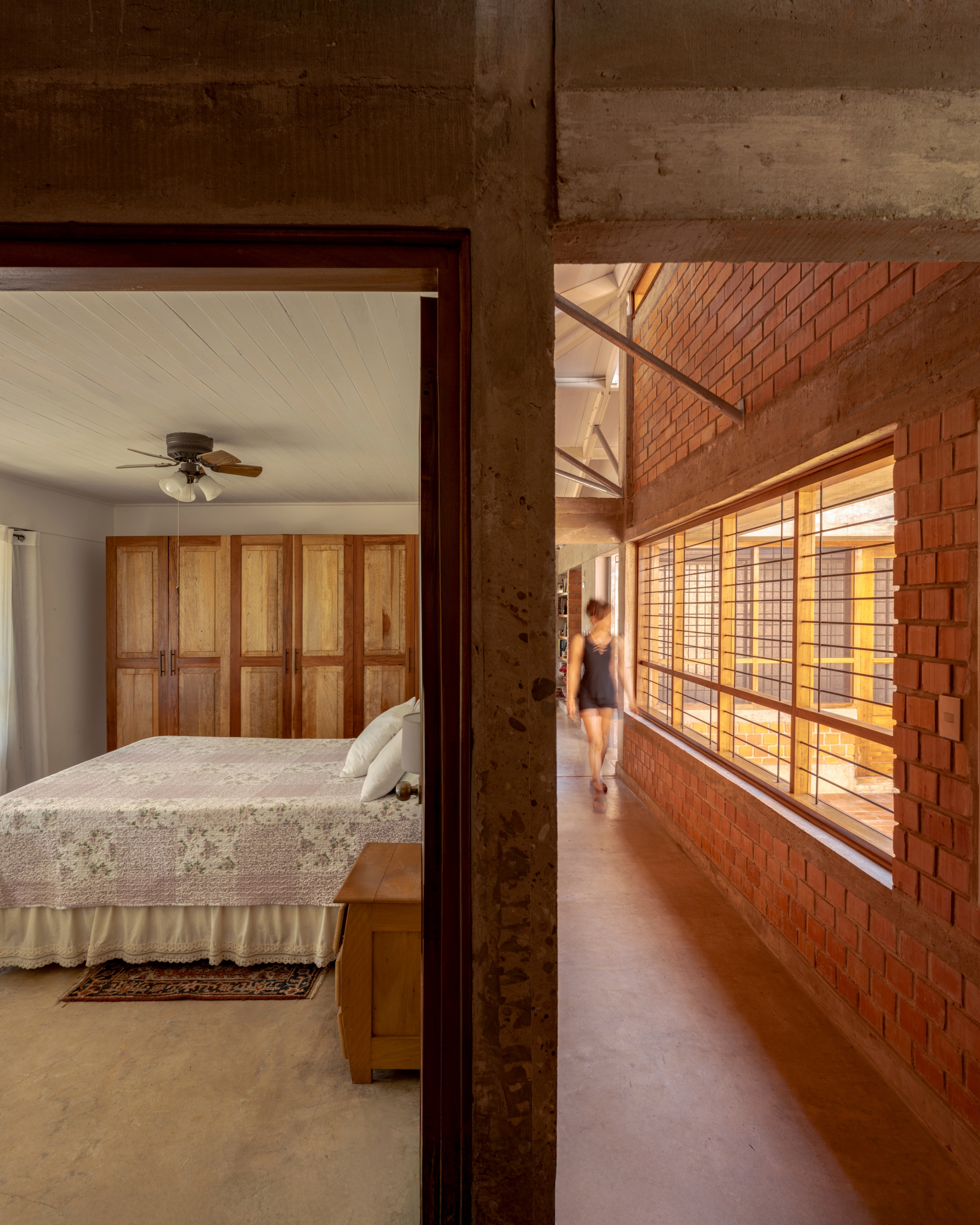 Hallway with latticed timber screens and concrete columns beside a bedroom doorway at dusk