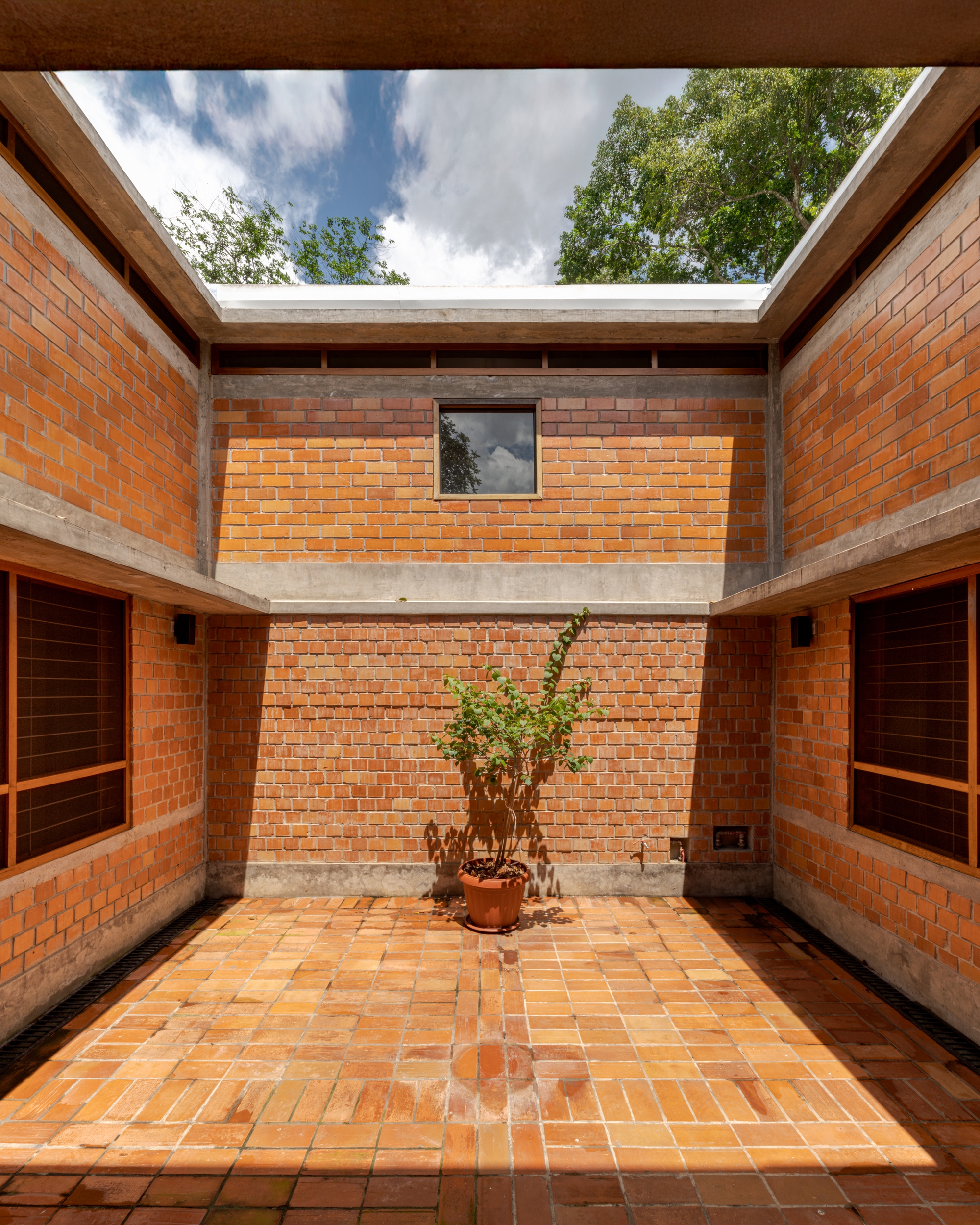 Interior courtyard with terracotta brick walls and tiled floor surrounding a potted plant under open sky