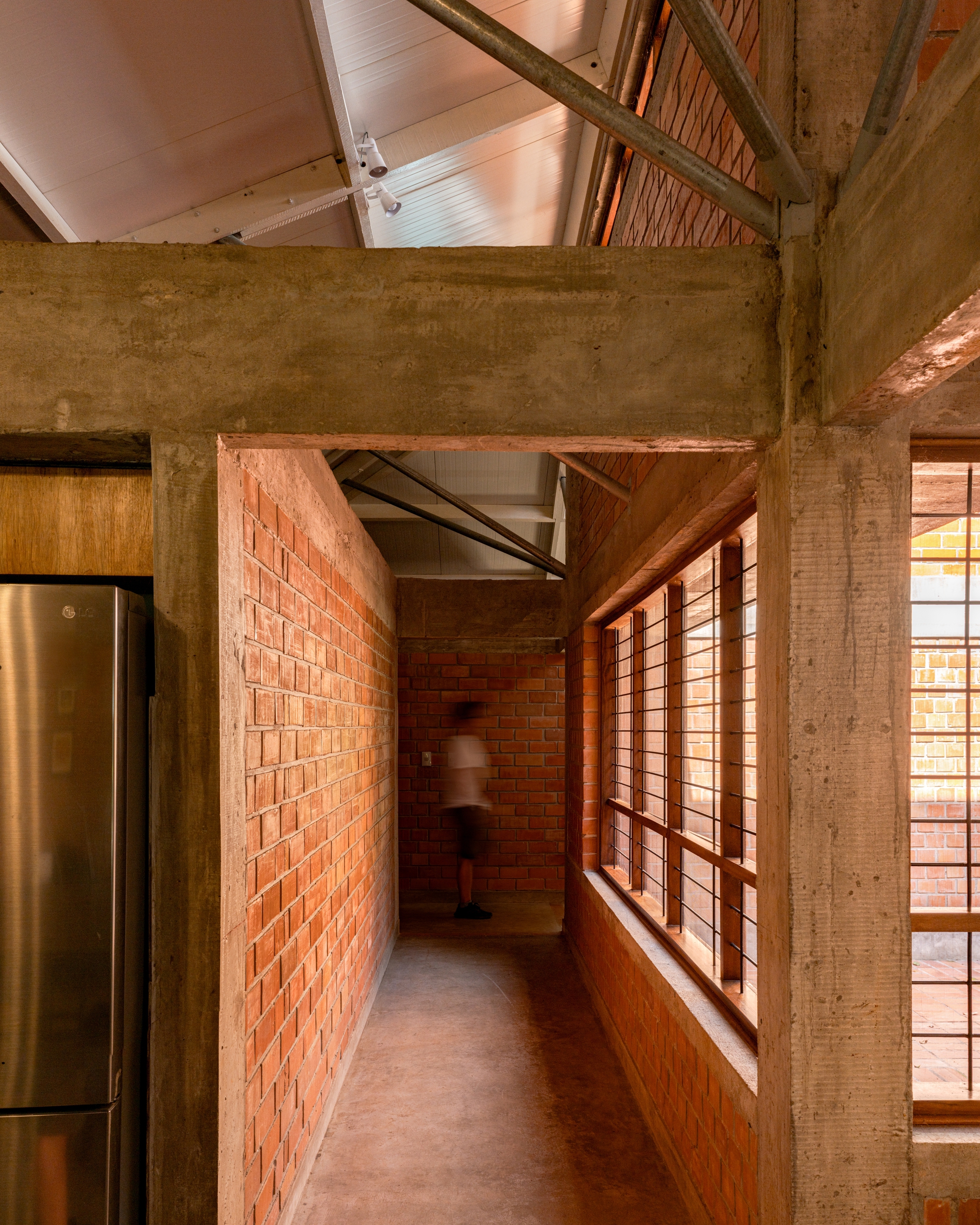Corridor with exposed brick wall and concrete beam framing a figure in motion beneath the roof structure
