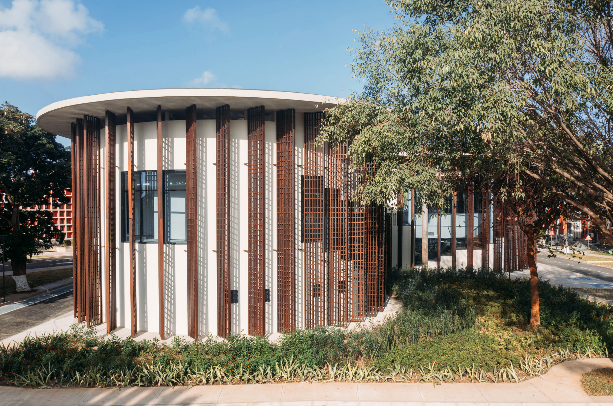Cylindrical pavilion with alternating vertical brick and perforated screen panels beneath a curved roof