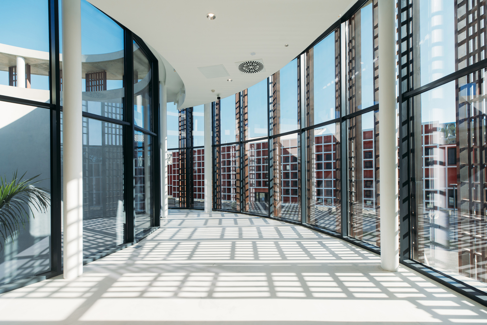 Interior corridor with floor-to-ceiling glass walls and patterned light cast by exterior screens