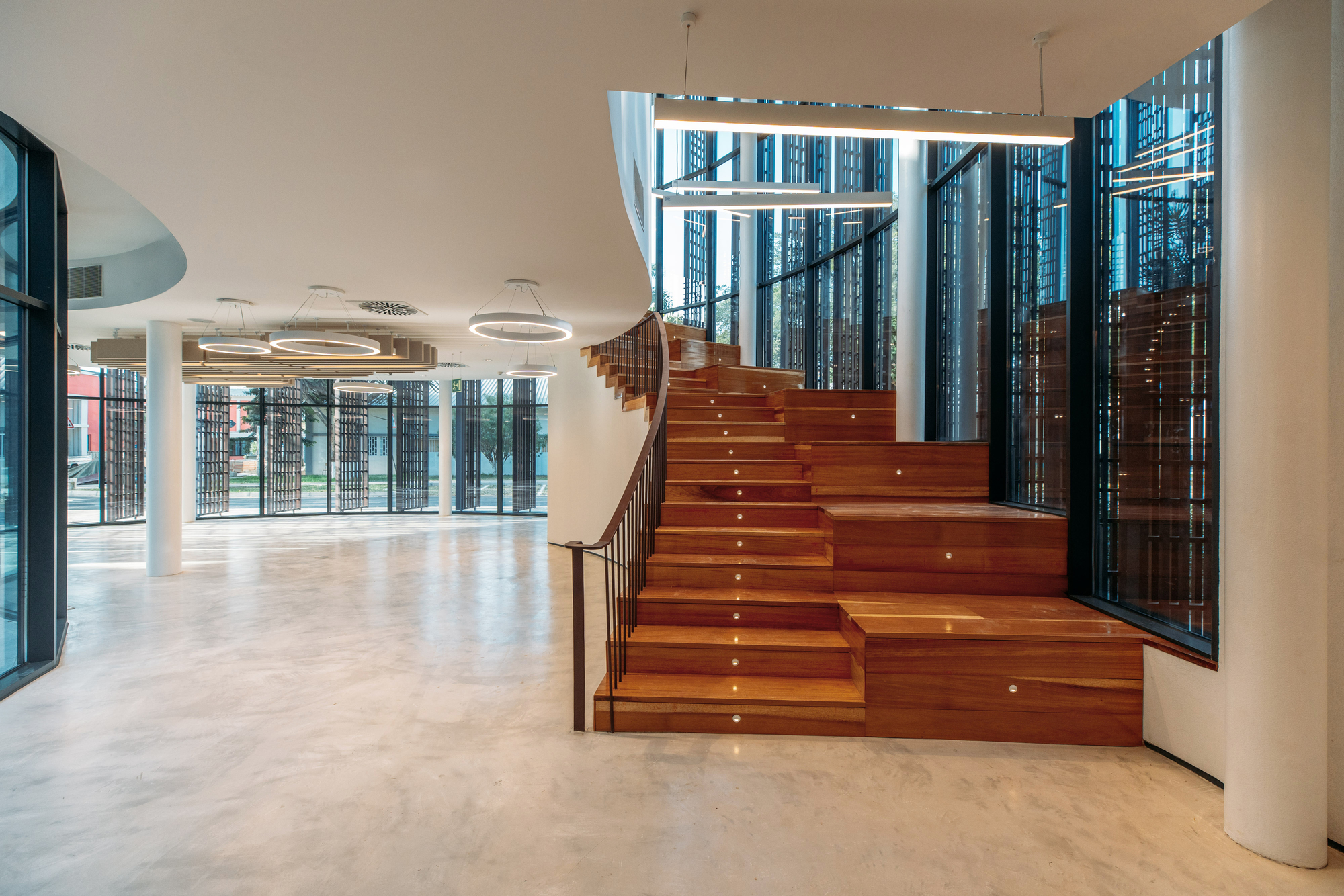 Wide timber staircase with recessed lighting rising beside floor-to-ceiling glazed screening panels