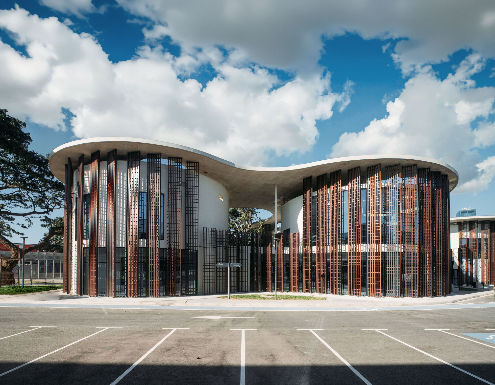 Curved facade with alternating terracotta and glass block screens under a concrete canopy roof