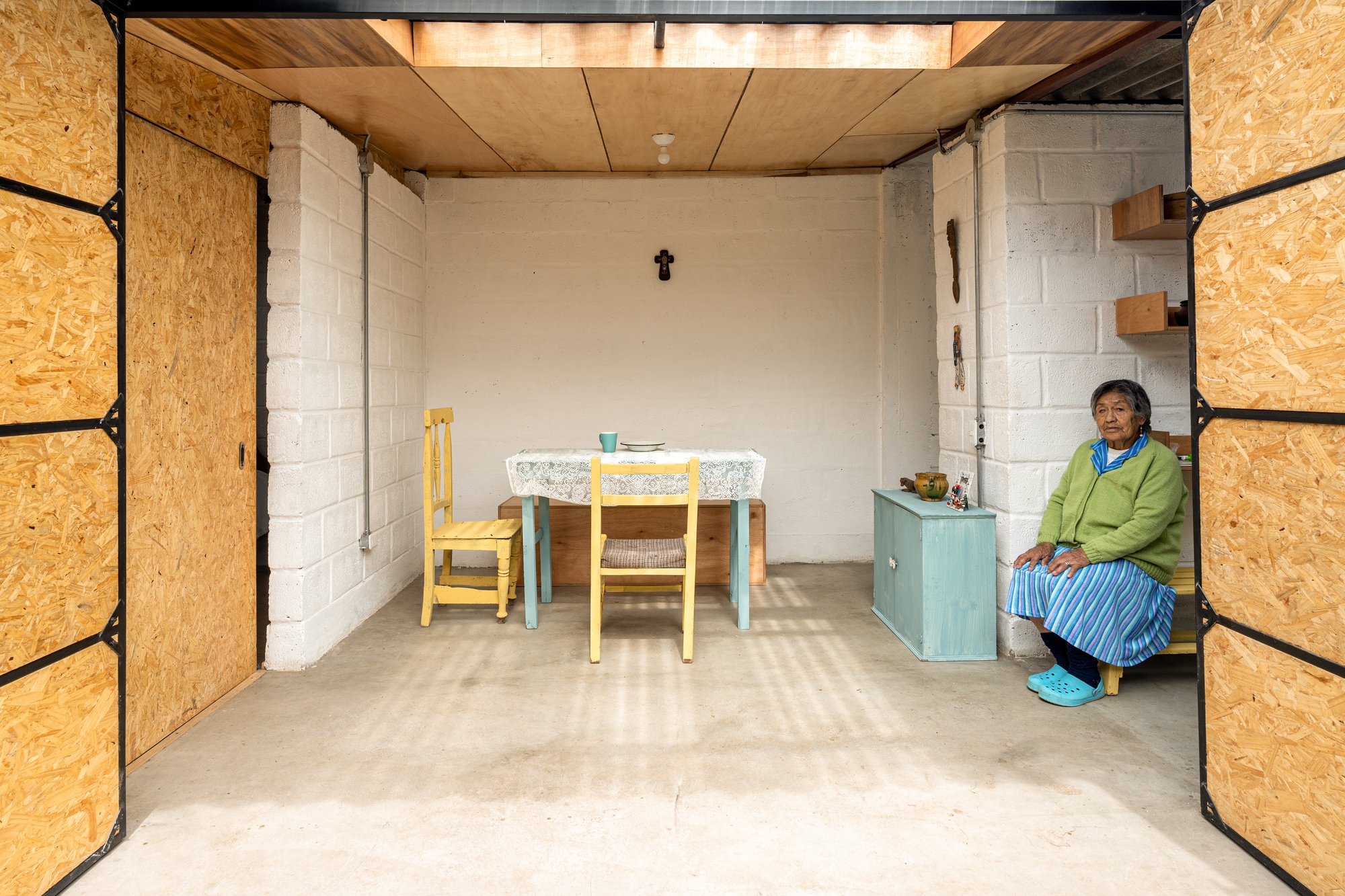 Interior living space with white painted concrete block walls and a woman seated in the corner