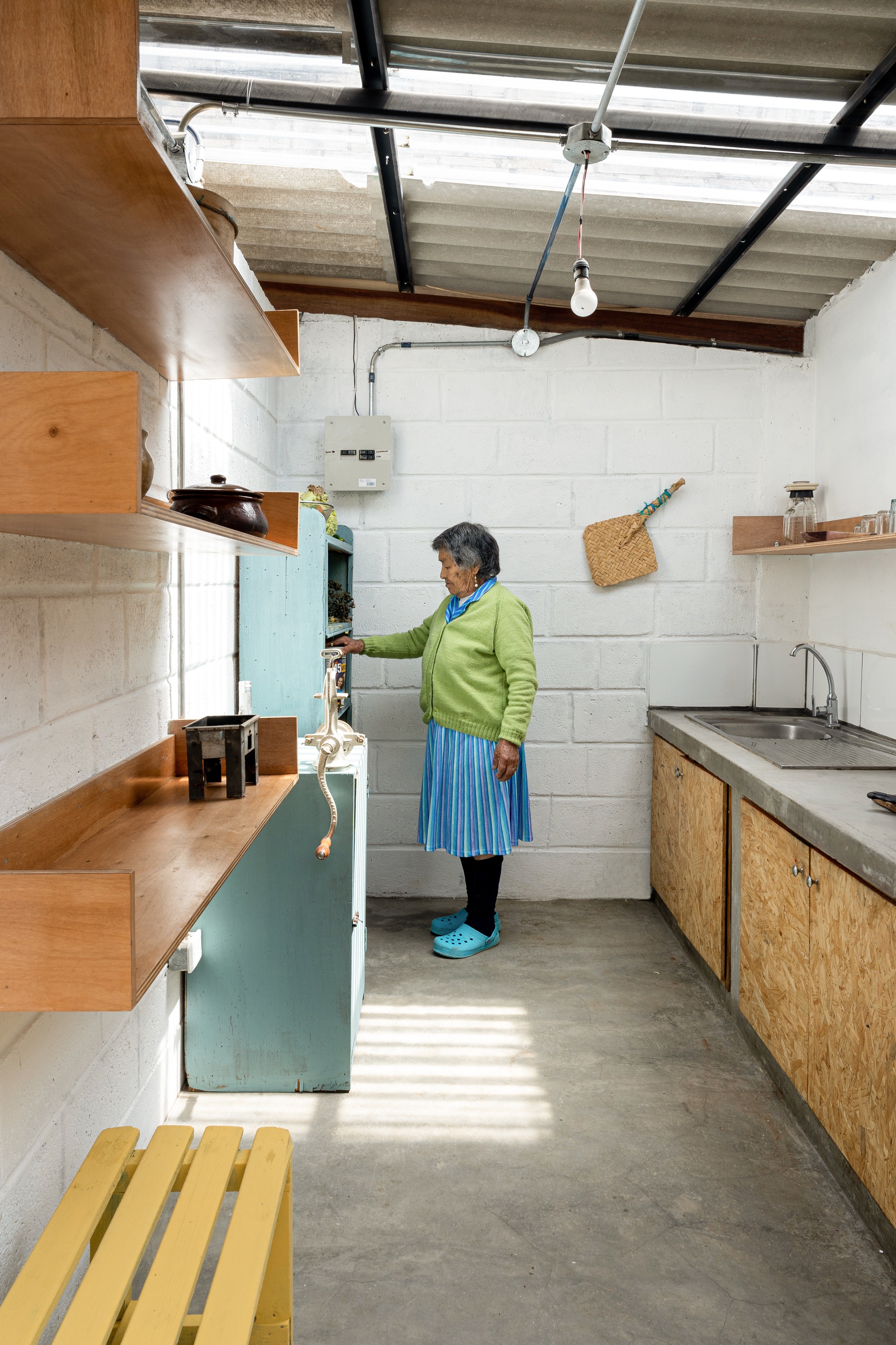 Compact kitchen with OSB cabinetry and a woman standing at the refrigerator under natural light