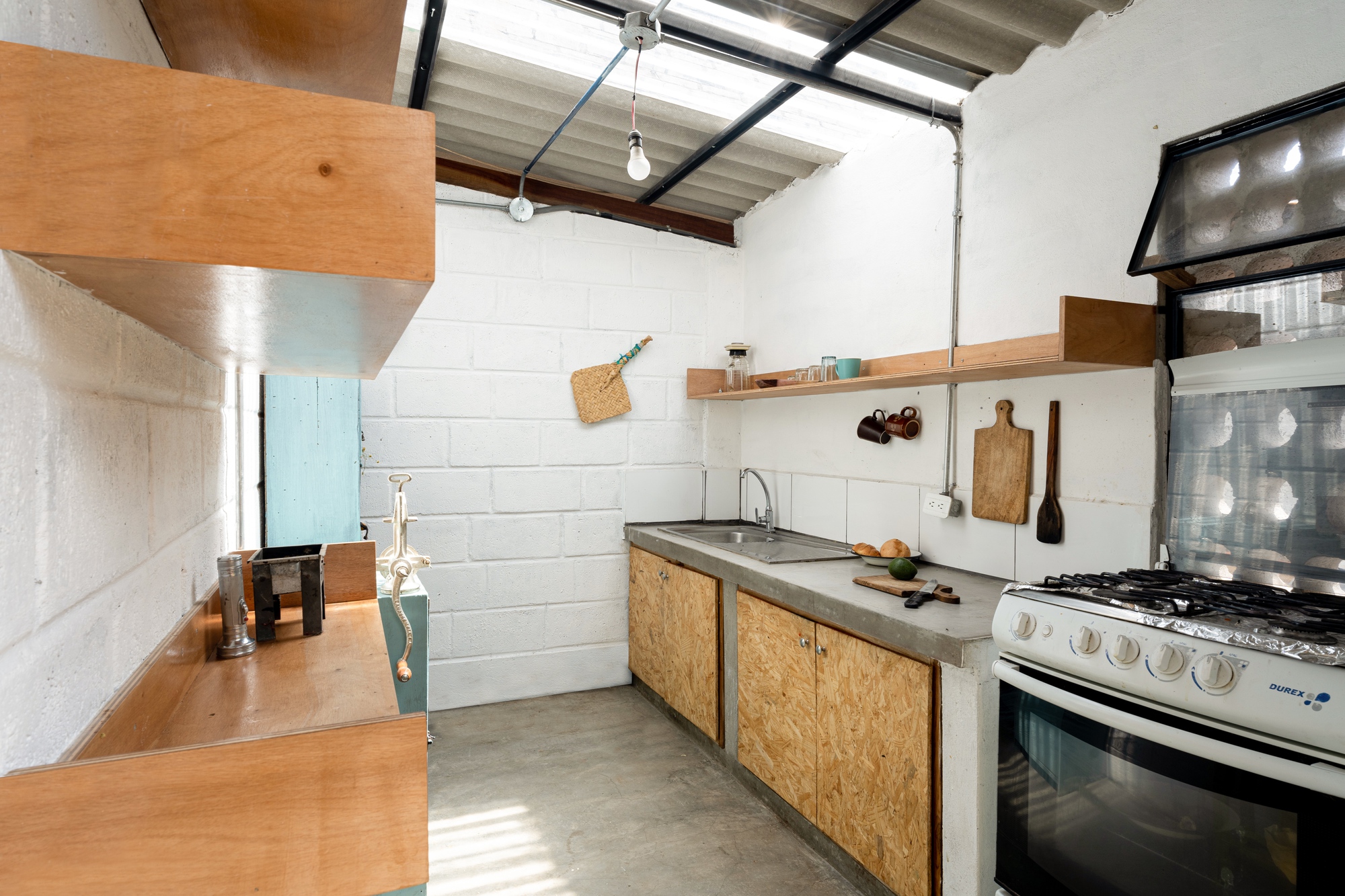 Kitchen counter with OSB base cabinets and concrete countertop below a corrugated skylight