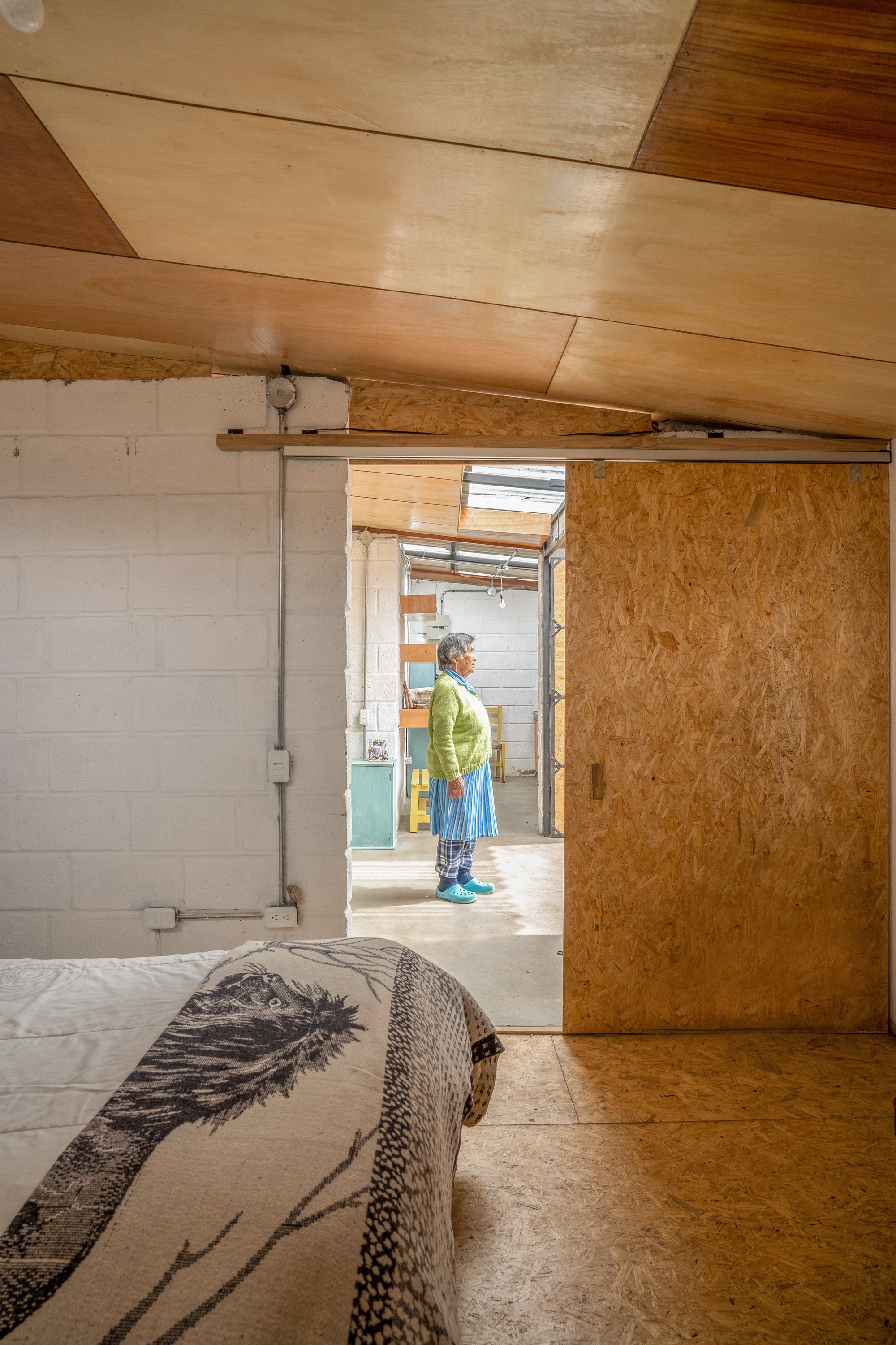 View through a sliding OSB door into the kitchen with a woman standing beyond