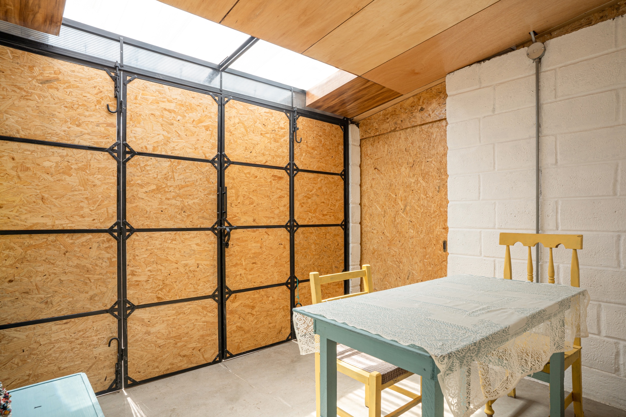 Interior dining area with OSB panel door and steel frame under plywood ceiling and skylight