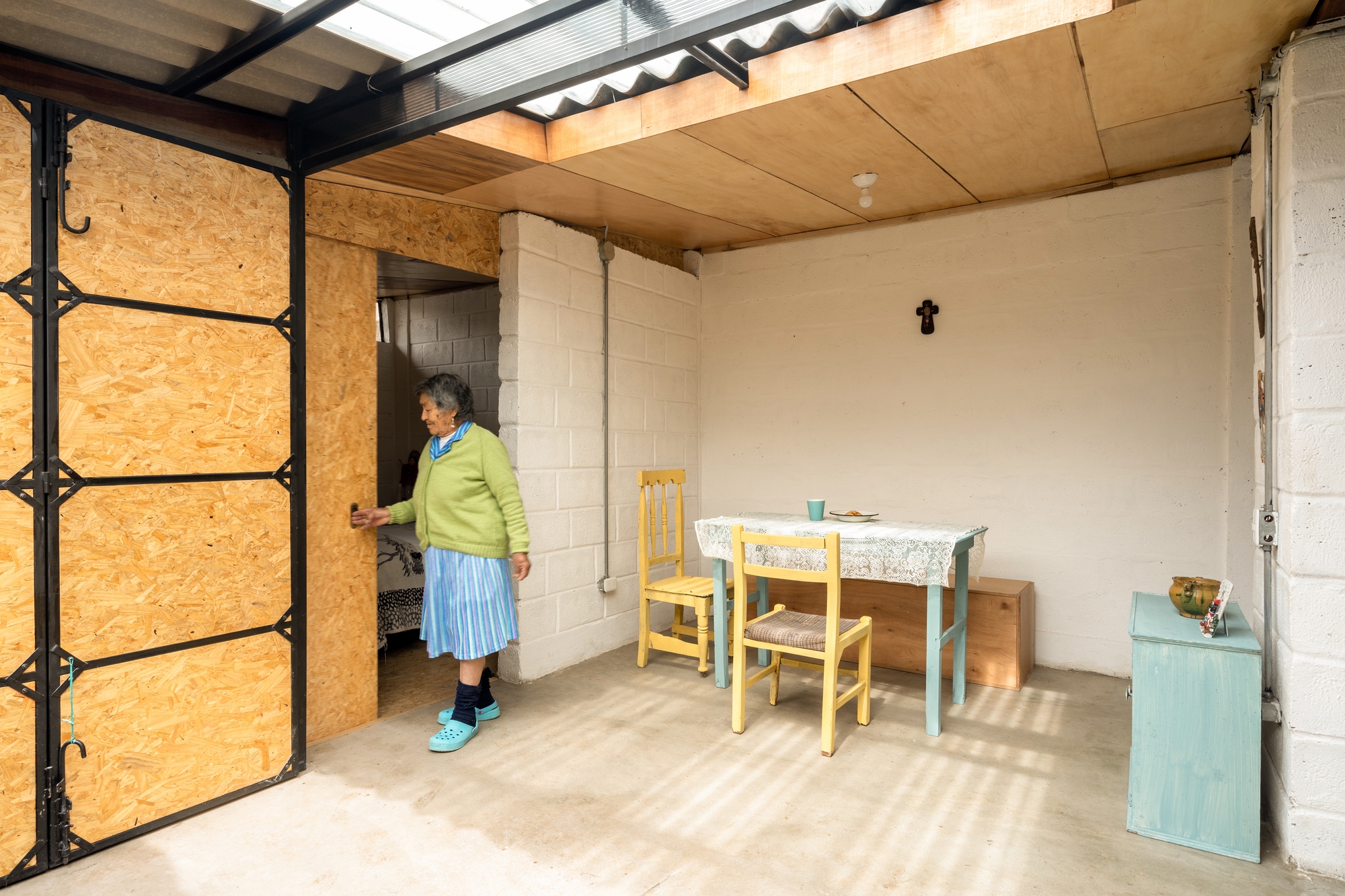 Living space with OSB panel door open revealing a resident in green sweater walking through