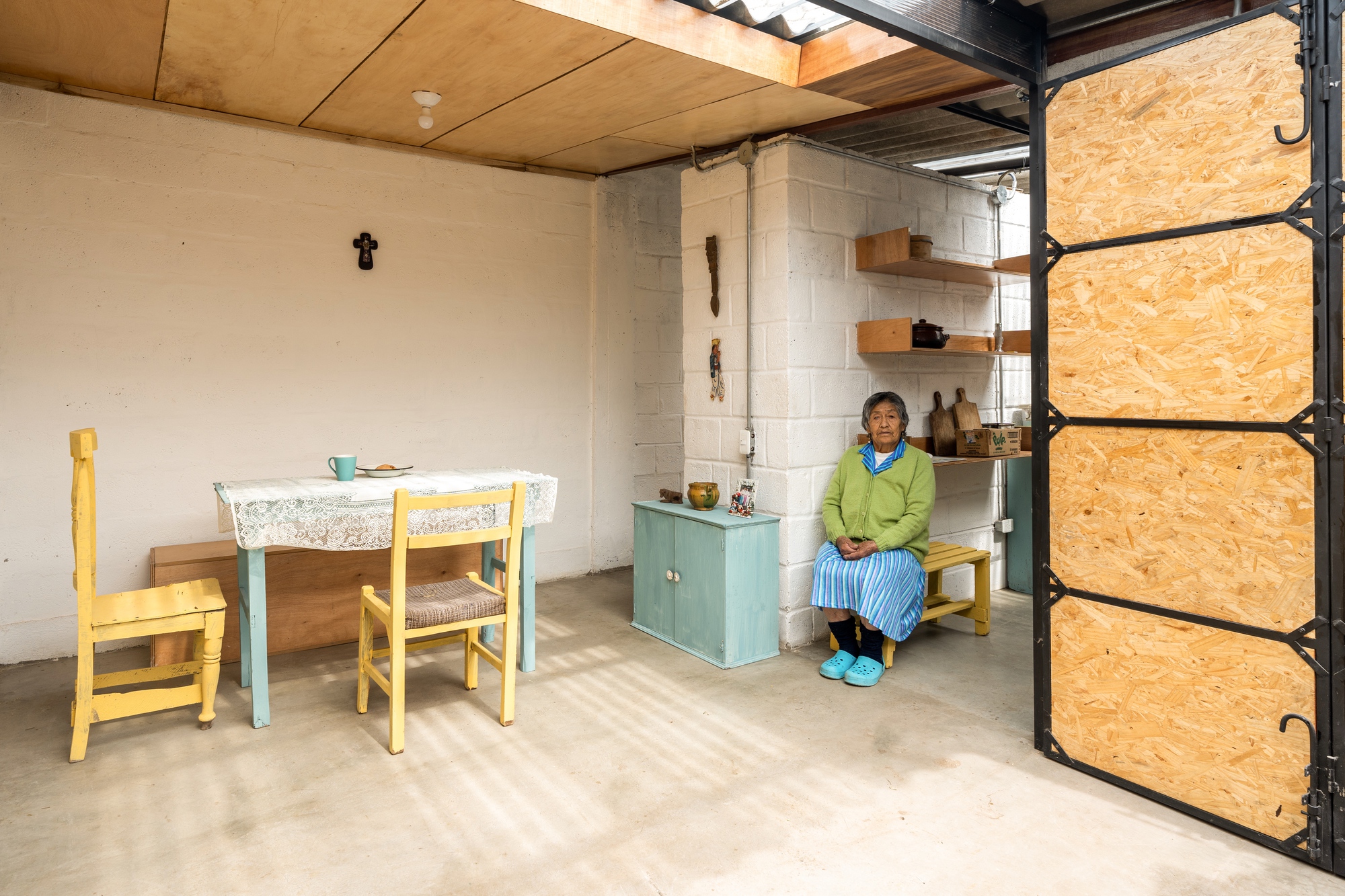 Dining area with exposed corrugated metal roofing and resident seated beside open OSB door