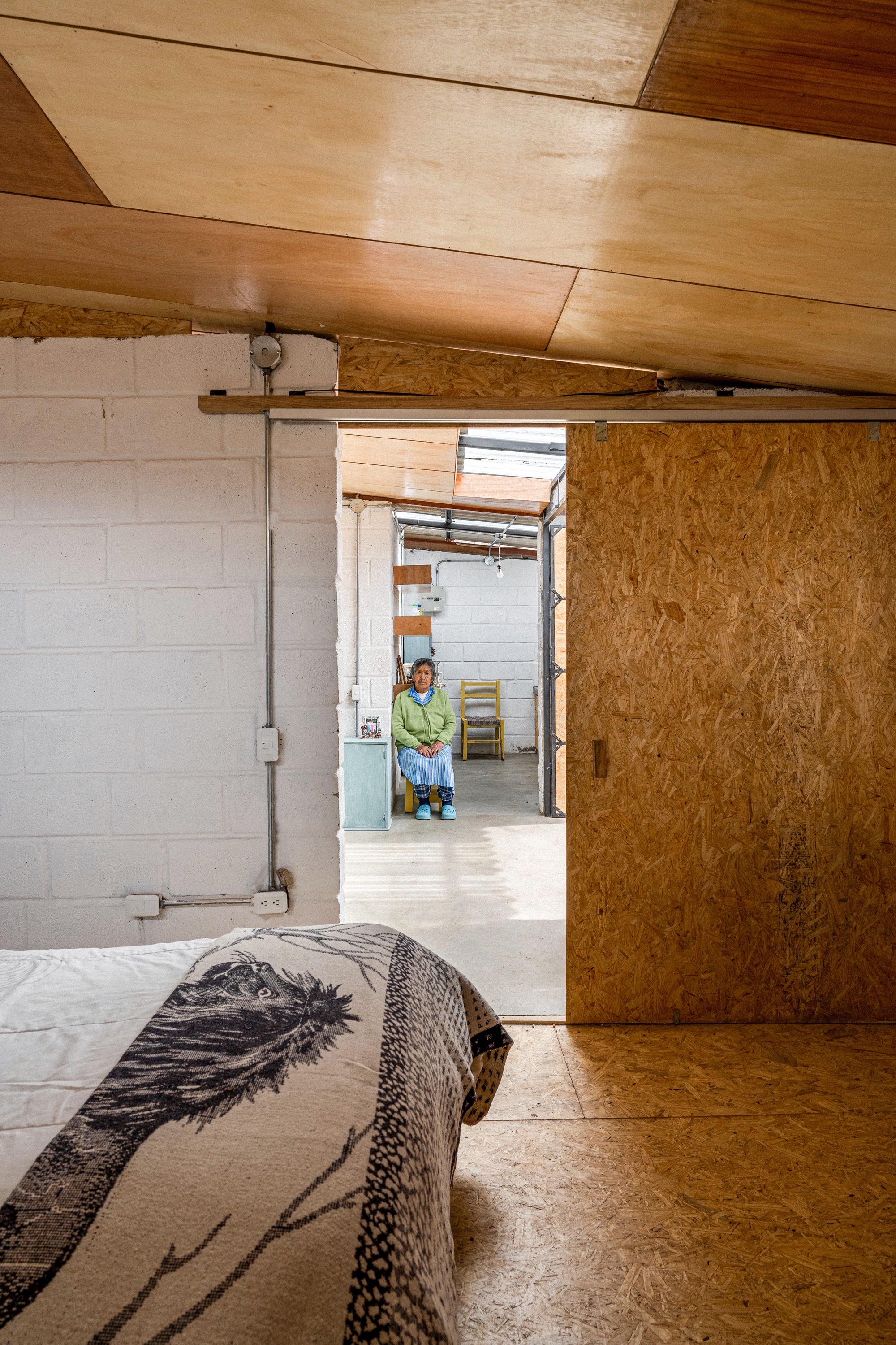 View through sliding OSB door from bedroom toward living area with resident seated in distance