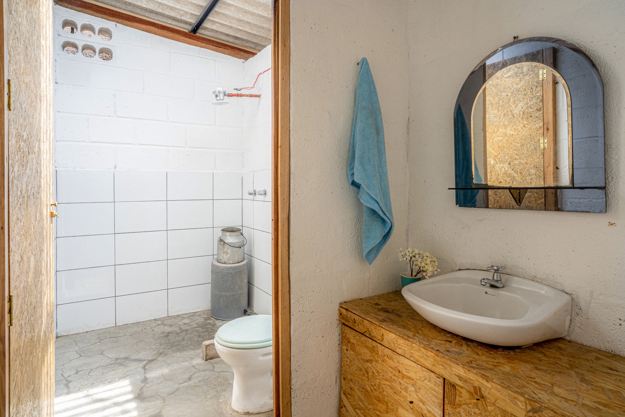 Bathroom with white tile walls, timber vanity, arched mirror, and view into adjacent shower room with corrugated ceiling