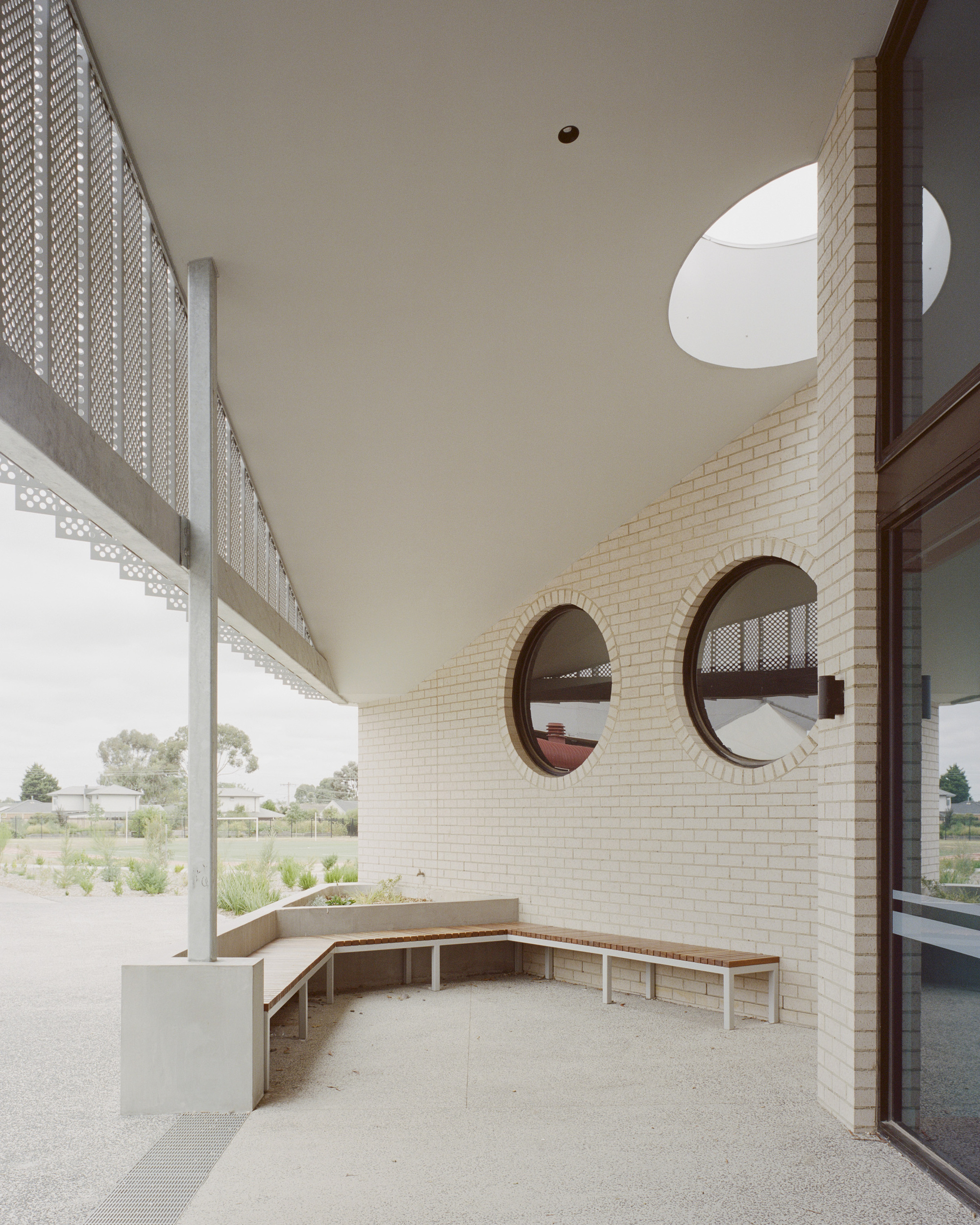 Covered courtyard with timber bench seating and circular openings in the brick wall above