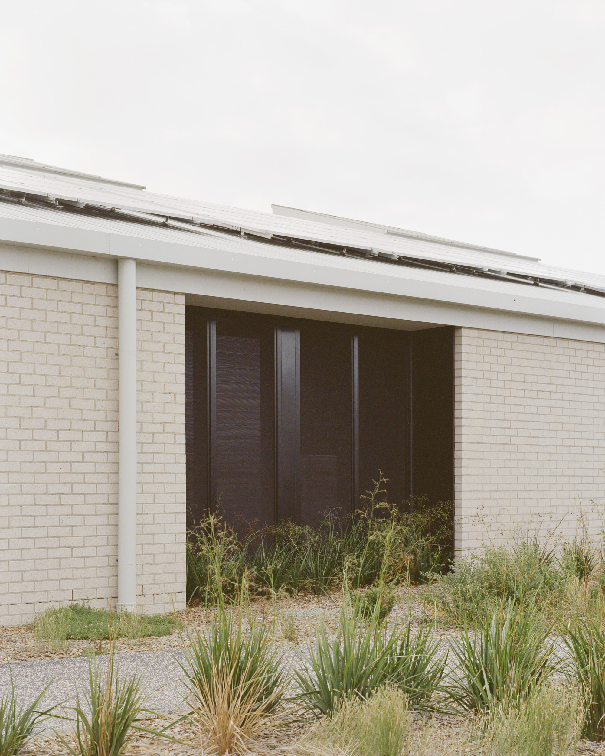 Recessed entry with dark timber doors set within pale brick walls and sheltered by a sloped metal roof
