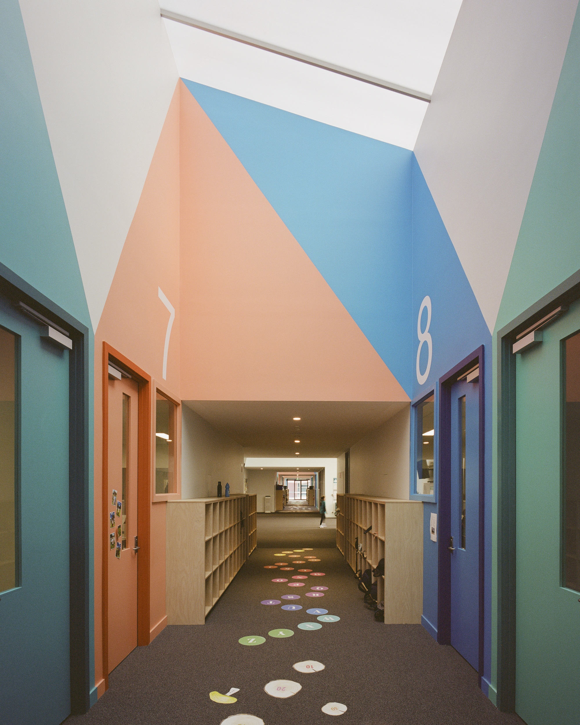 Interior corridor with vaulted ceiling painted in peach and blue geometric panels and colorful floor decals below skylights