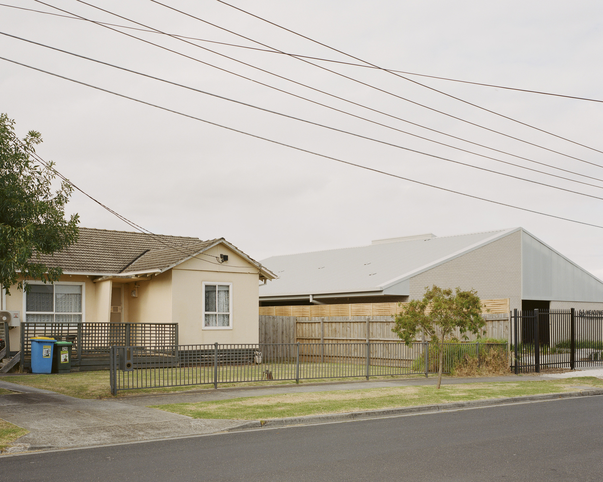 Street view of the white gabled volume beside an existing house with overhead power lines