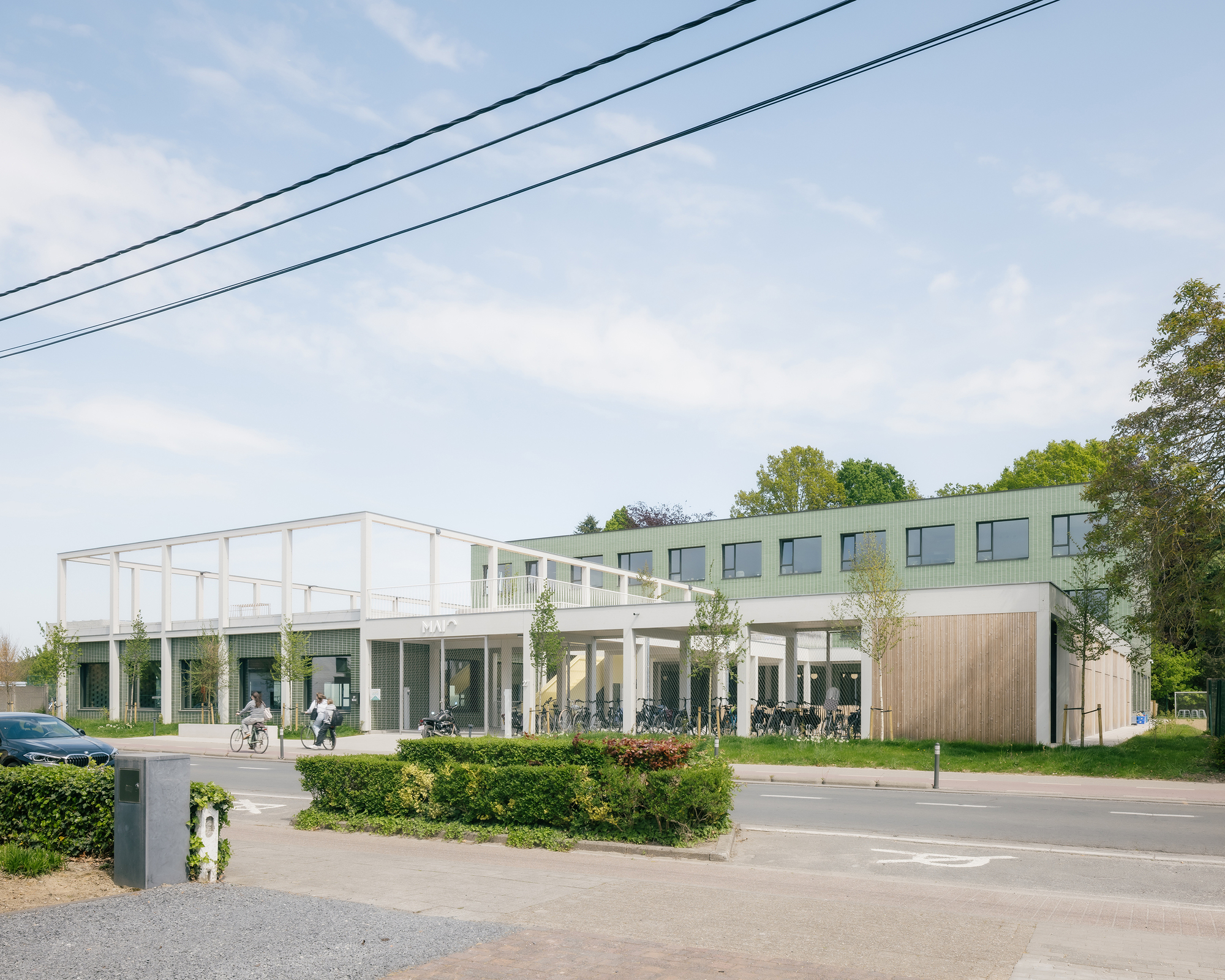Street view of the two-story building with green upper facade and white colonnade beneath spring trees