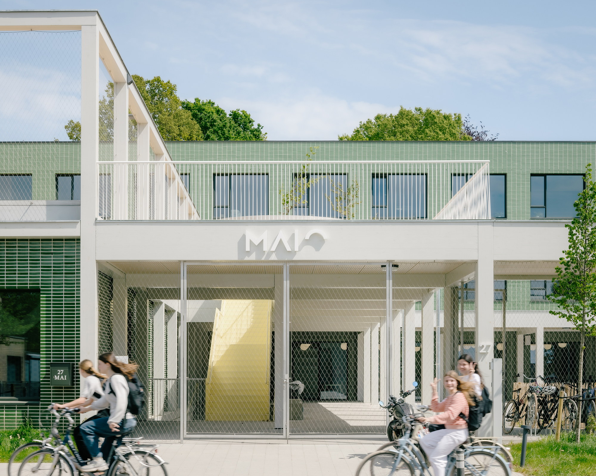 Entrance portico with white steel frame and mesh screens as cyclists pass in motion