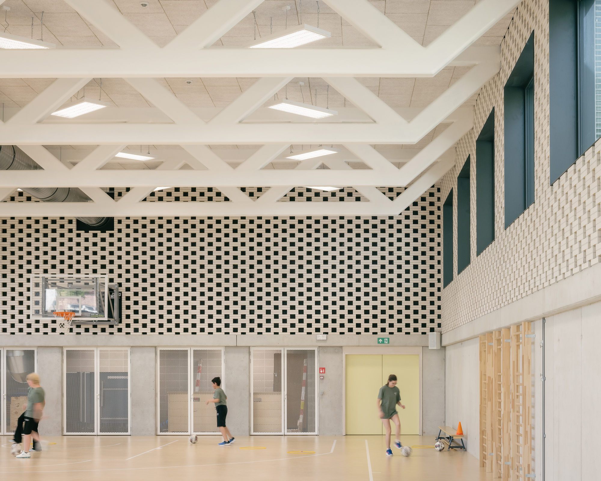 Interior sports hall with white lattice truss roof and perforated brick wall panels