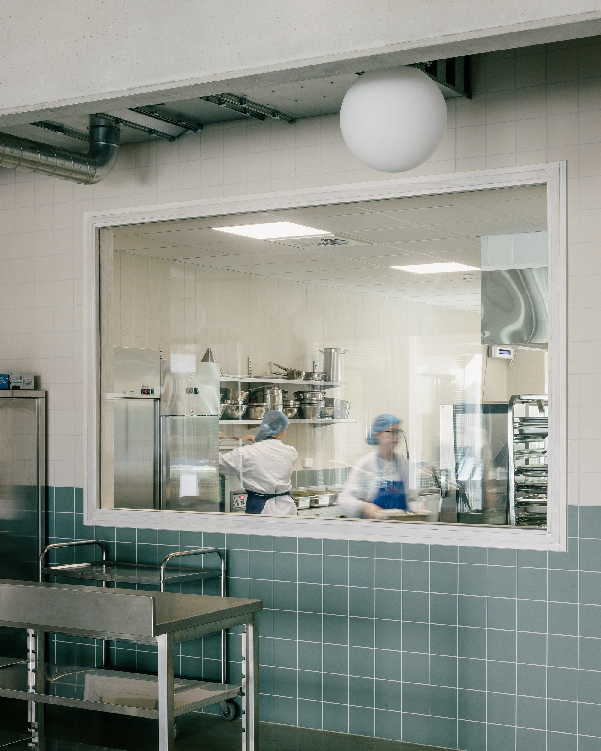 Kitchen pass-through window framed in white with teal tile surround and workers in motion