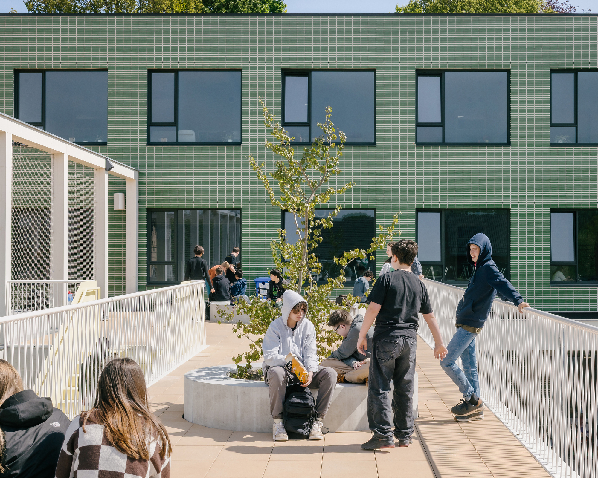 Rooftop terrace with concrete planters, young trees and students gathering under bright midday sun