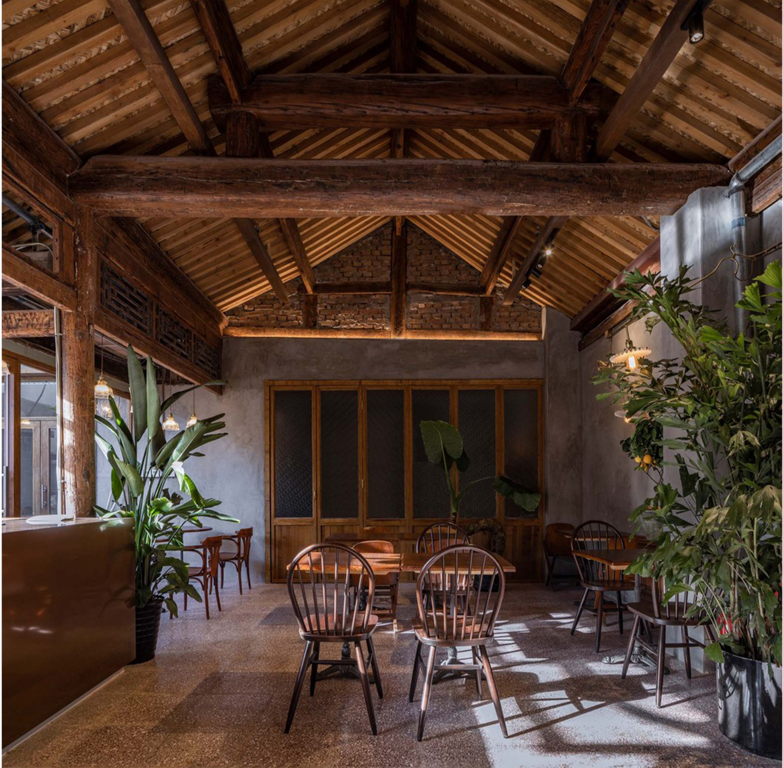 Warm café seating framed by exposed timber trusses, brick walls, and indoor greenery.