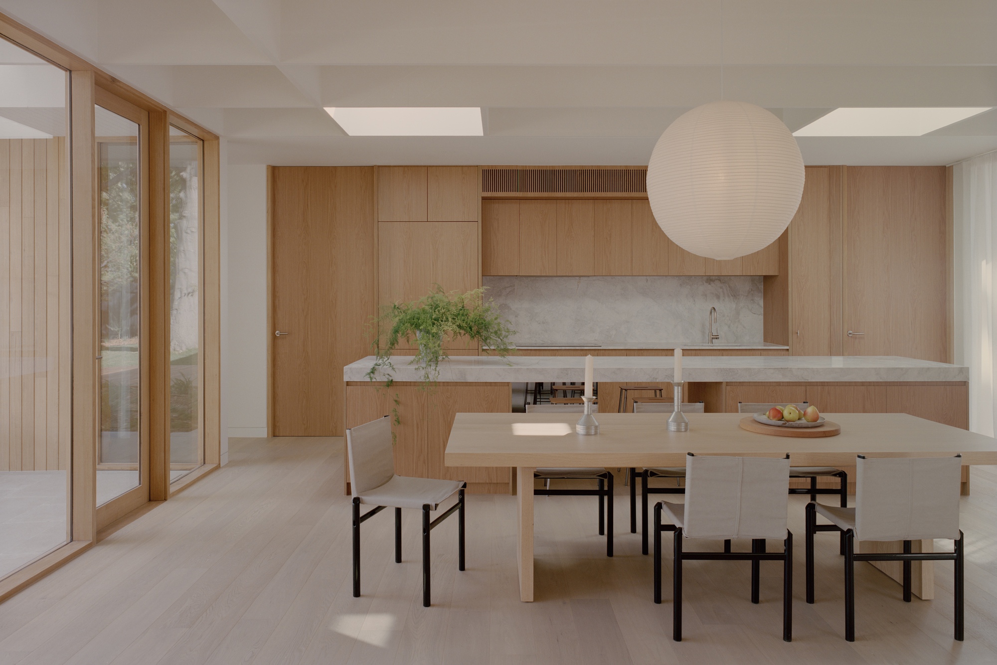 Open kitchen and dining space with timber cabinetry and skylights casting afternoon shadows