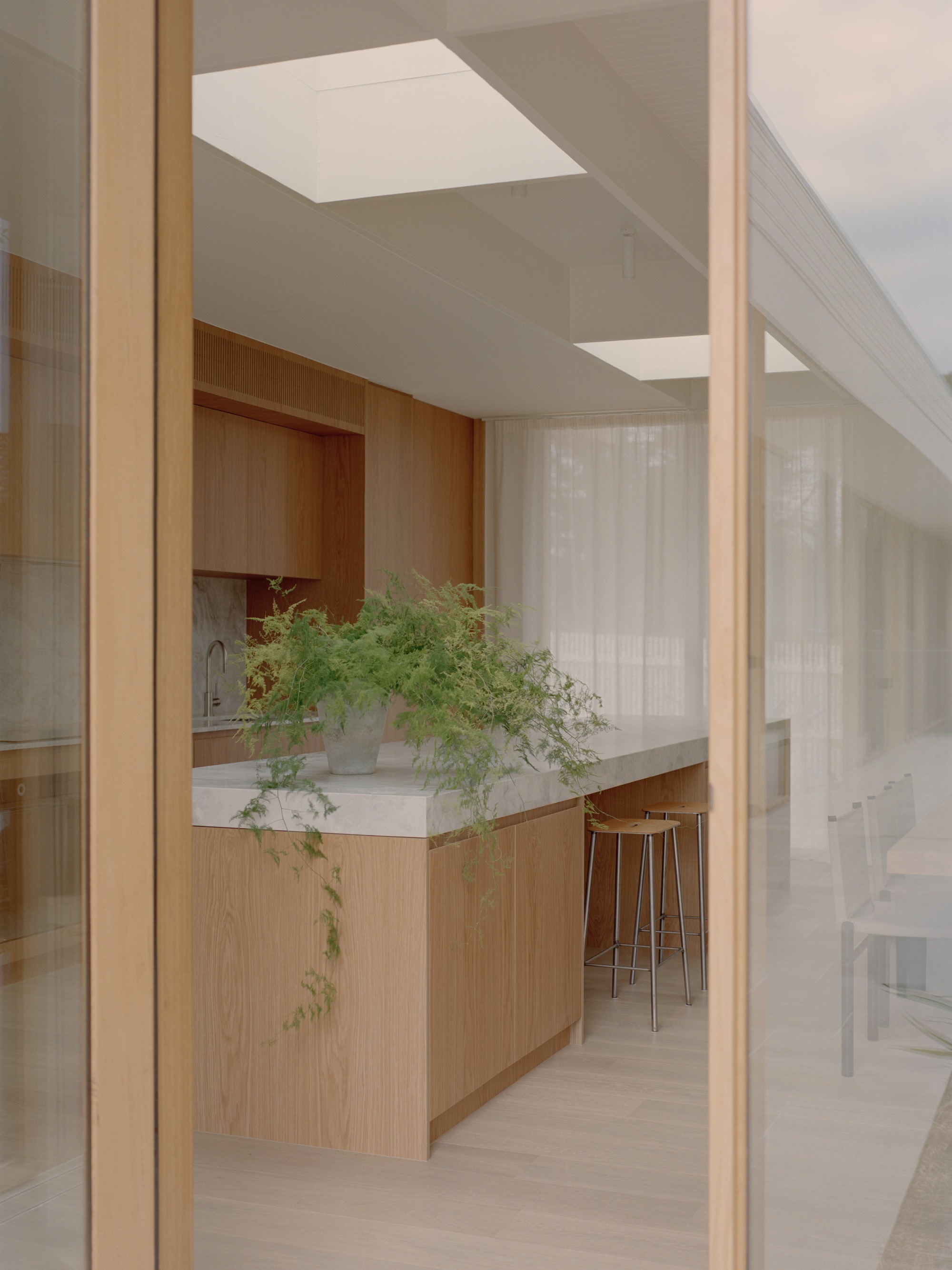 Kitchen island with potted trailing plant viewed through timber-framed glass door