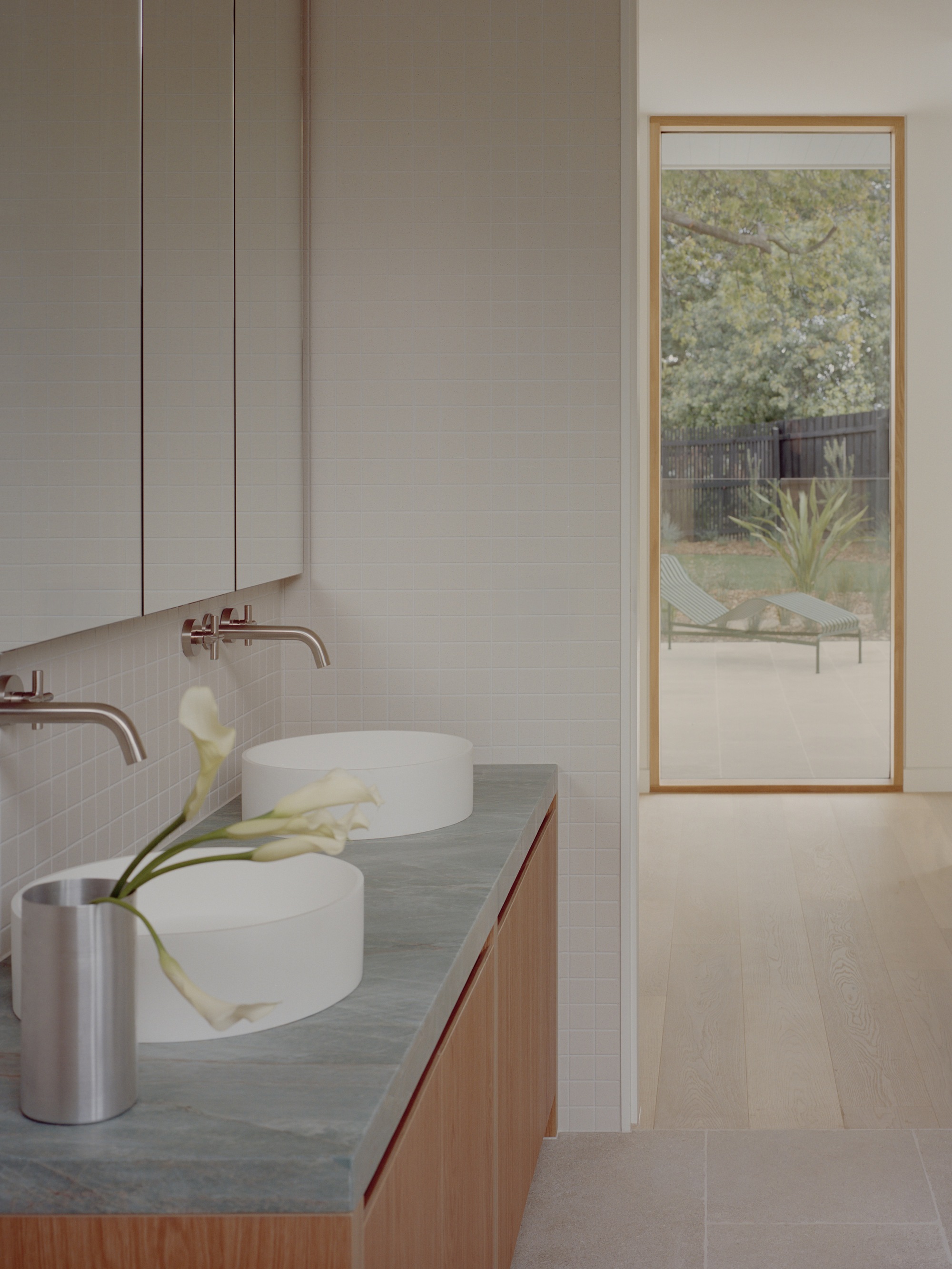 Bathroom vanity with twin vessel sinks and timber-framed window overlooking a garden courtyard