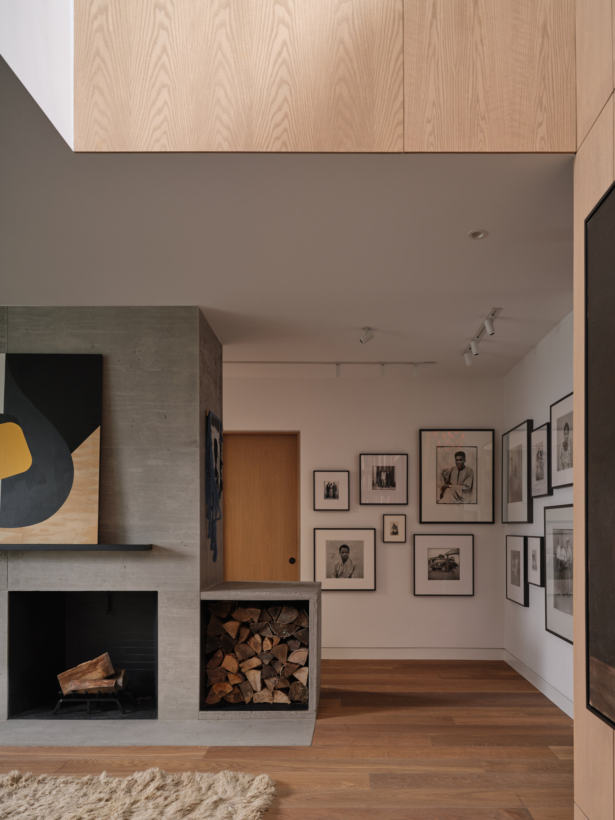 Double-height living room with concrete fireplace, firewood niche, and gallery wall of framed photographs