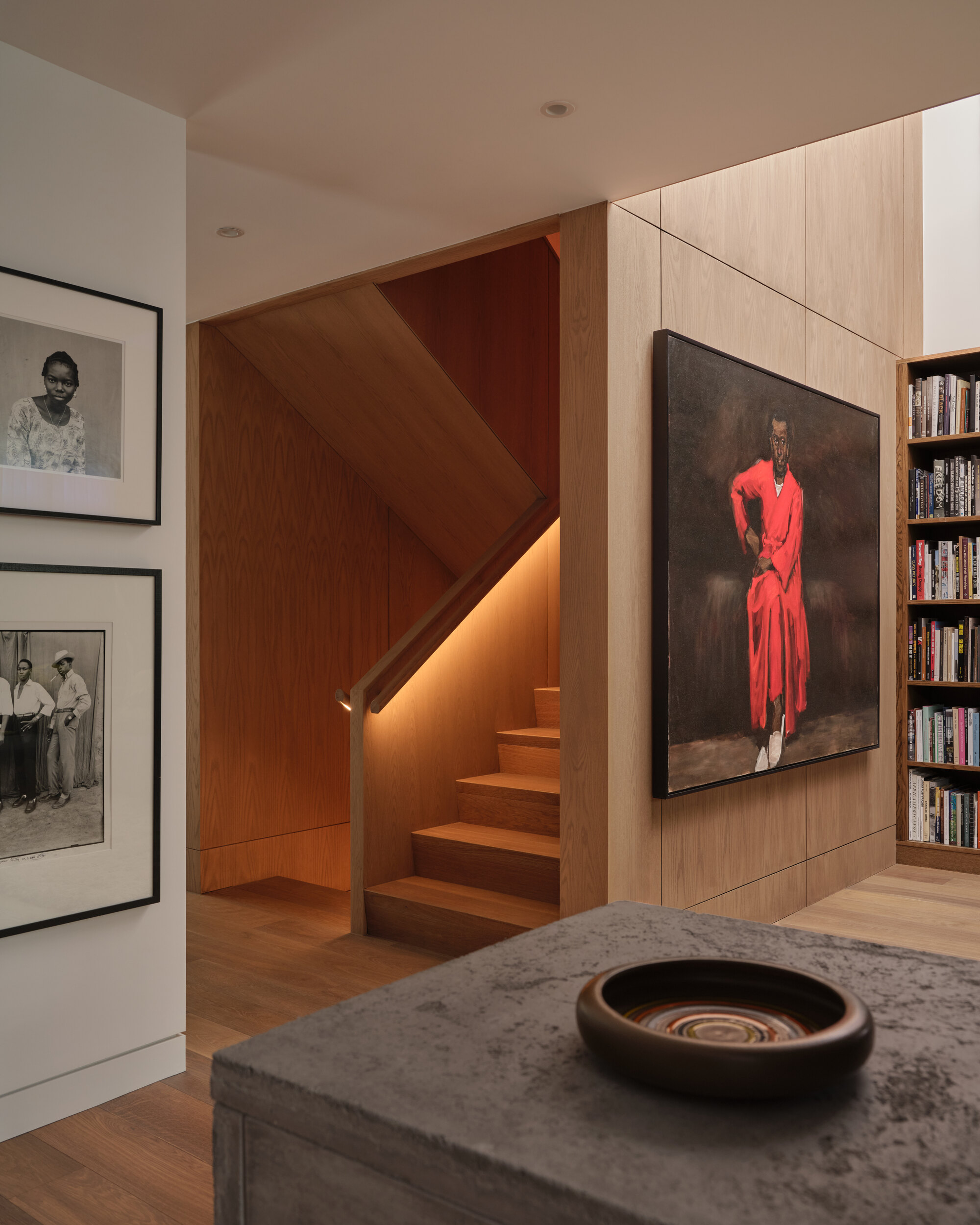 Timber-clad stairwell with integrated lighting beneath the treads and adjacent bookshelf