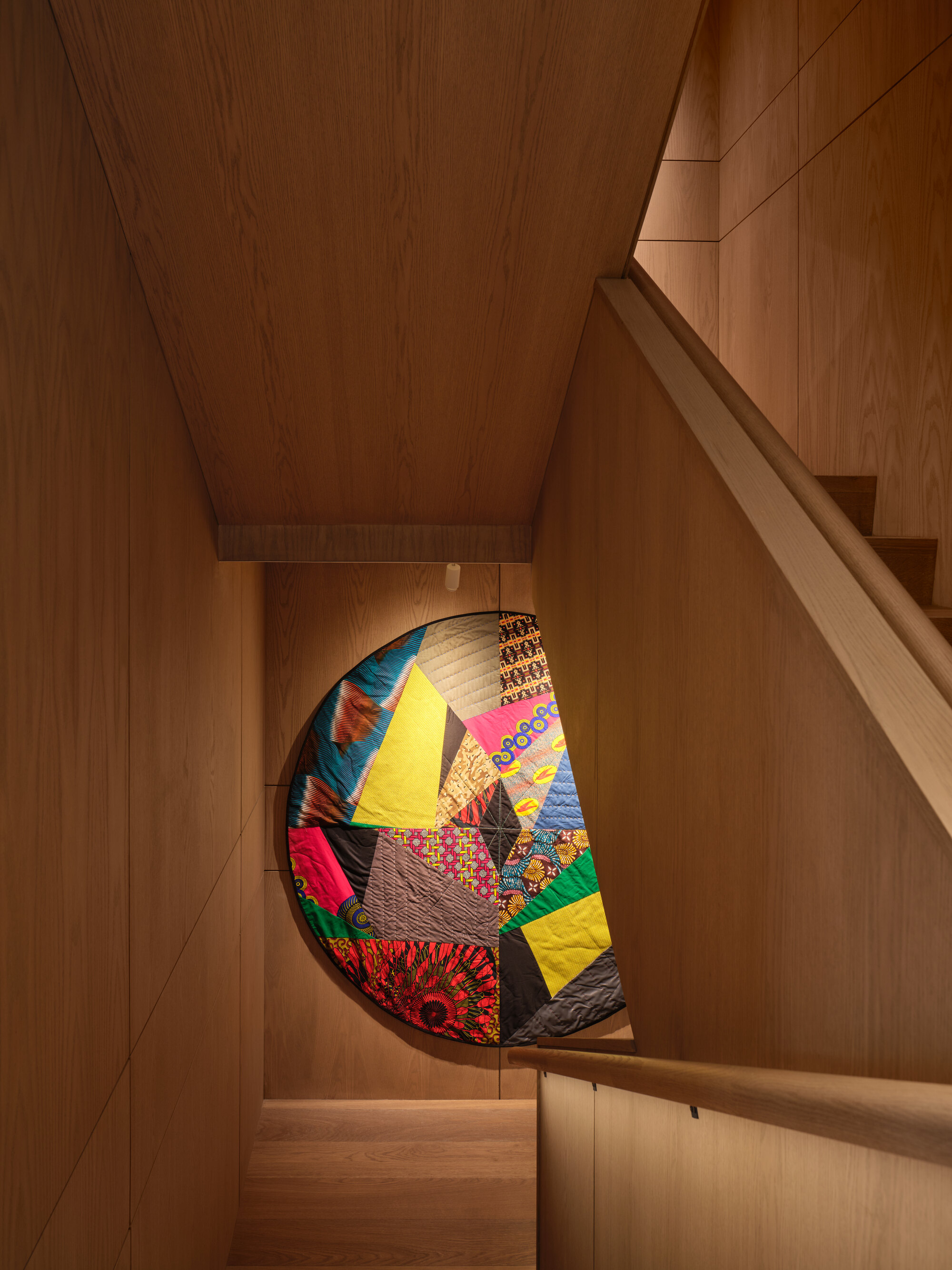 Wood-paneled staircase with patchwork quilt displayed in a recessed niche beneath the landing
