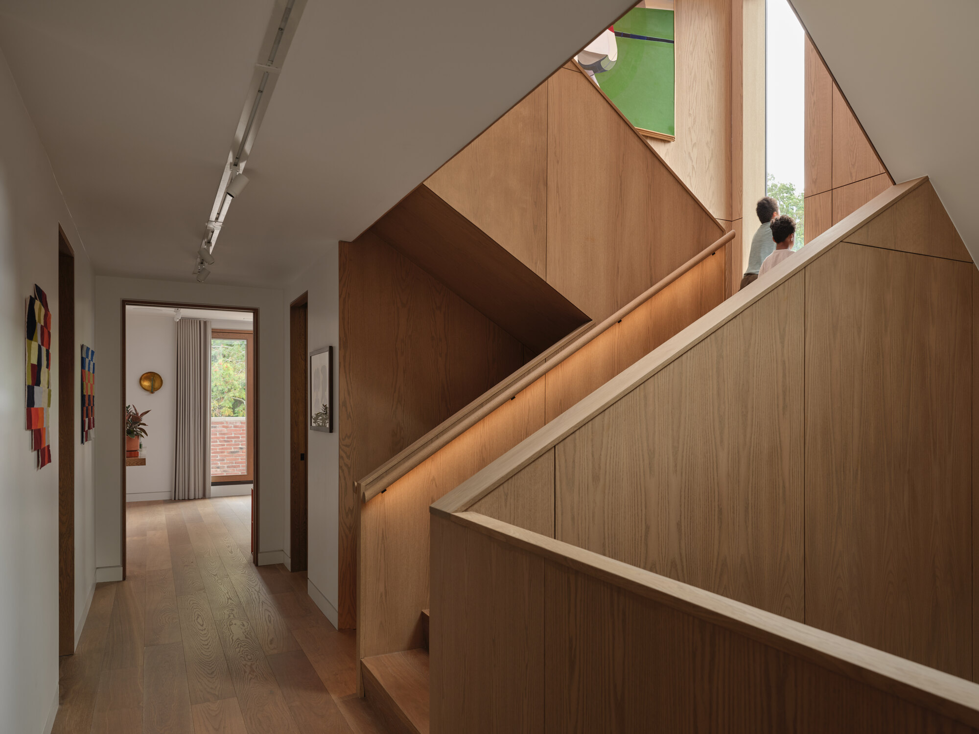 Oak staircase rising from hallway with two figures ascending toward a stained glass window