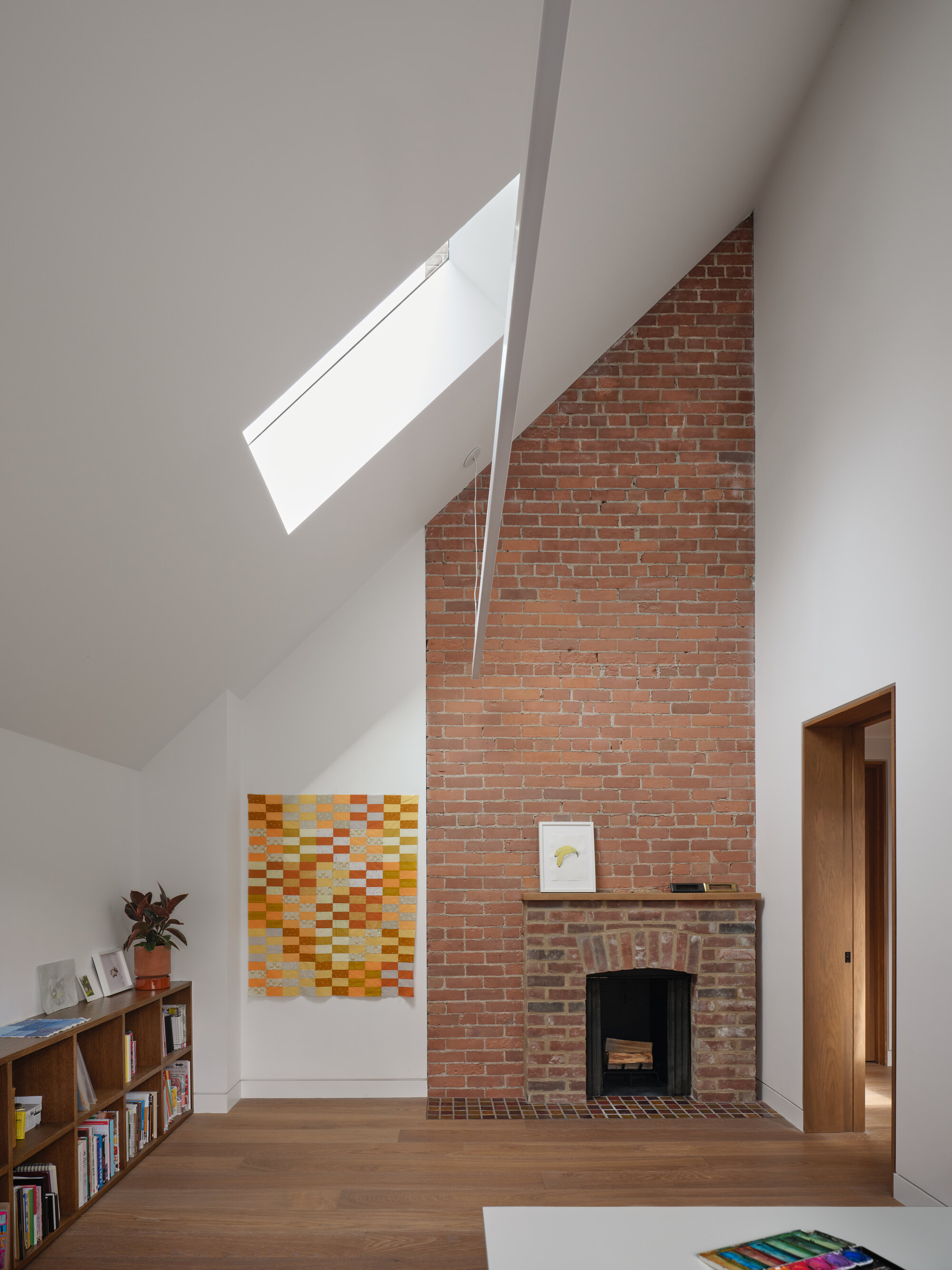 Exposed brick fireplace beneath a sloped ceiling with angled skylight illuminating the chimney wall