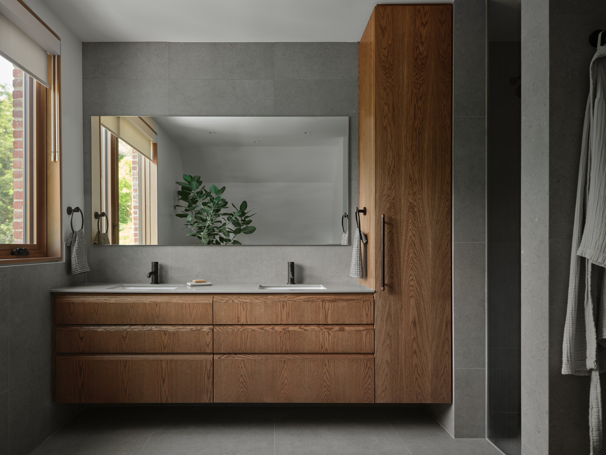 Floating timber vanity with dual sinks beneath a wide mirror in a grey-tiled bathroom