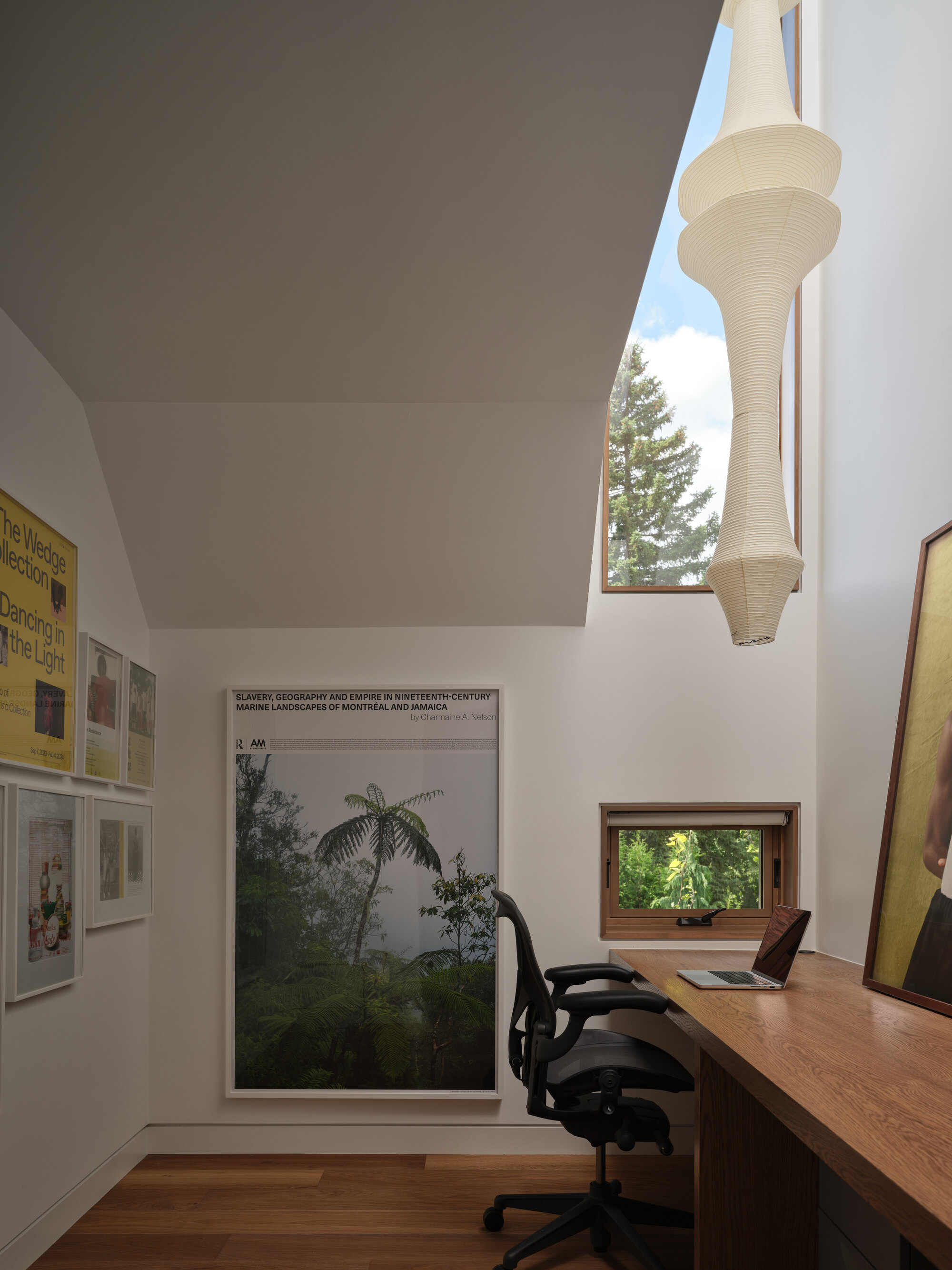 Double-height workspace with sculptural pendant light and horizontal window framing tree canopy