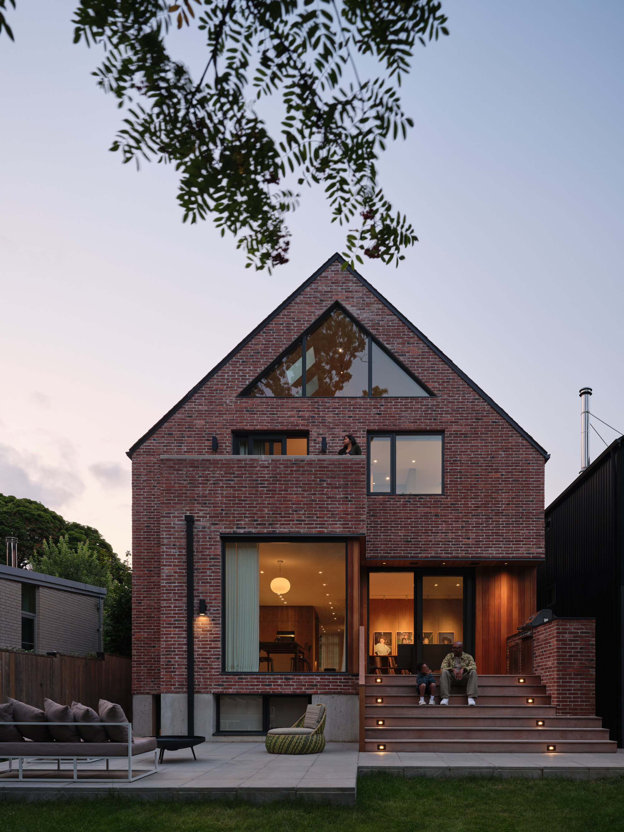 Red brick gable facade with glazed openings and timber deck at dusk