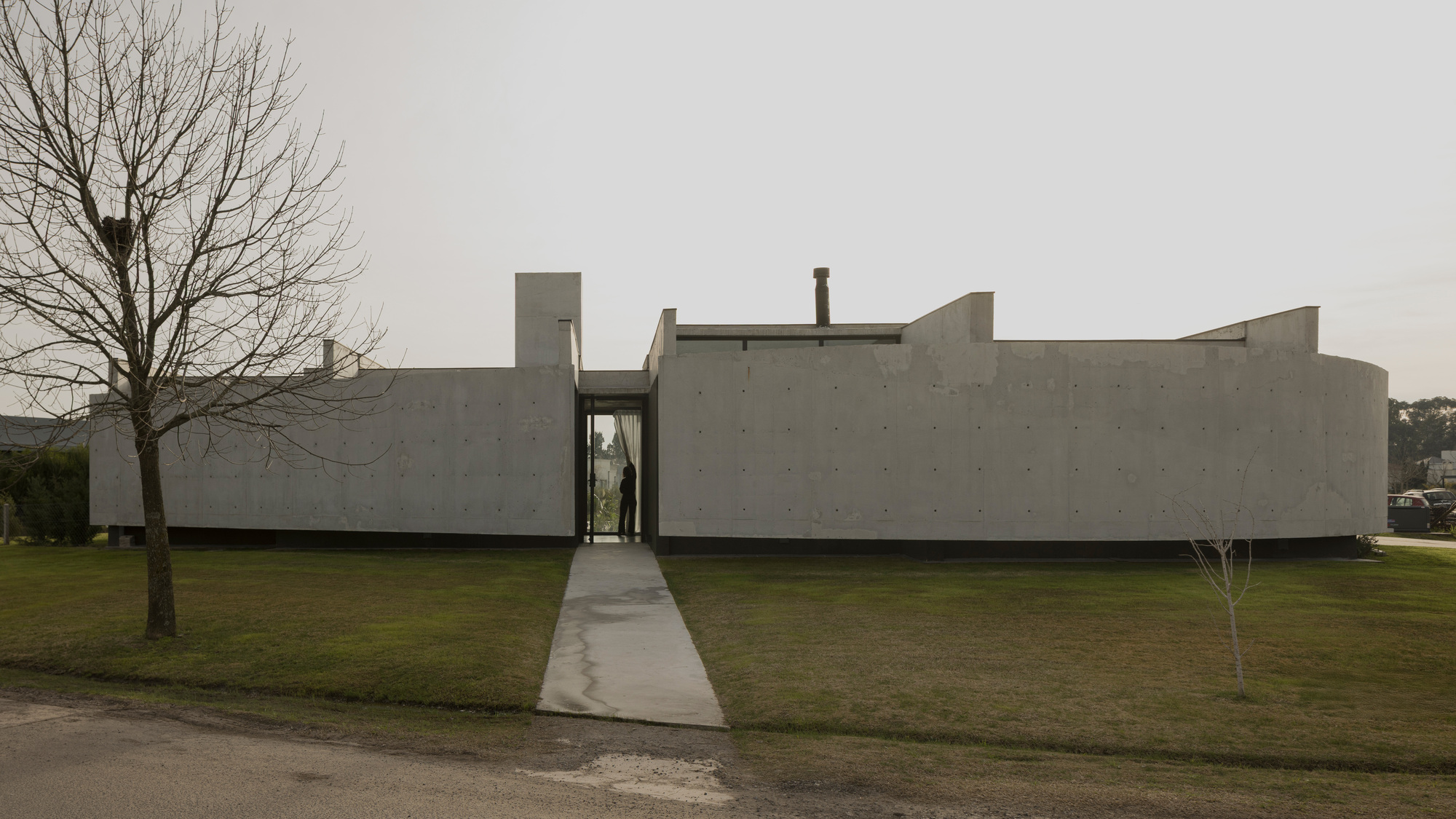 Concrete path leading to the recessed glass entry portal under an overcast sky