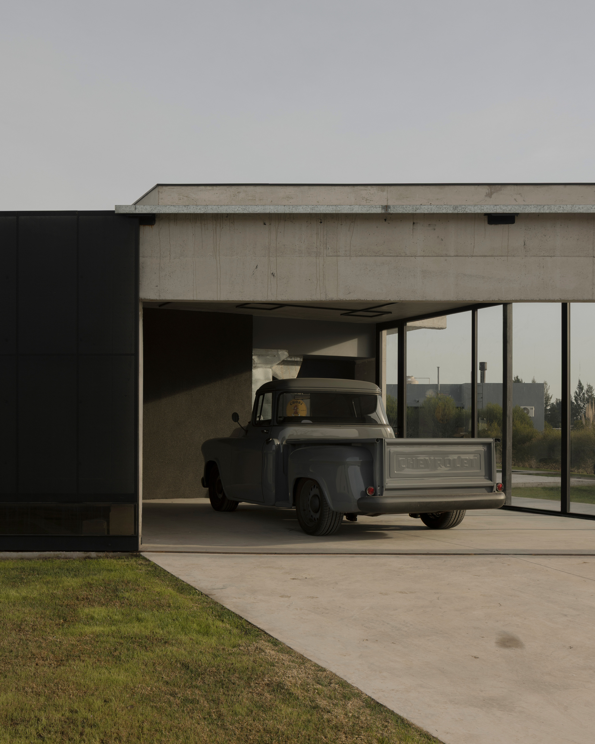 Carport with cantilevered concrete roof sheltering a vintage pickup truck at dusk