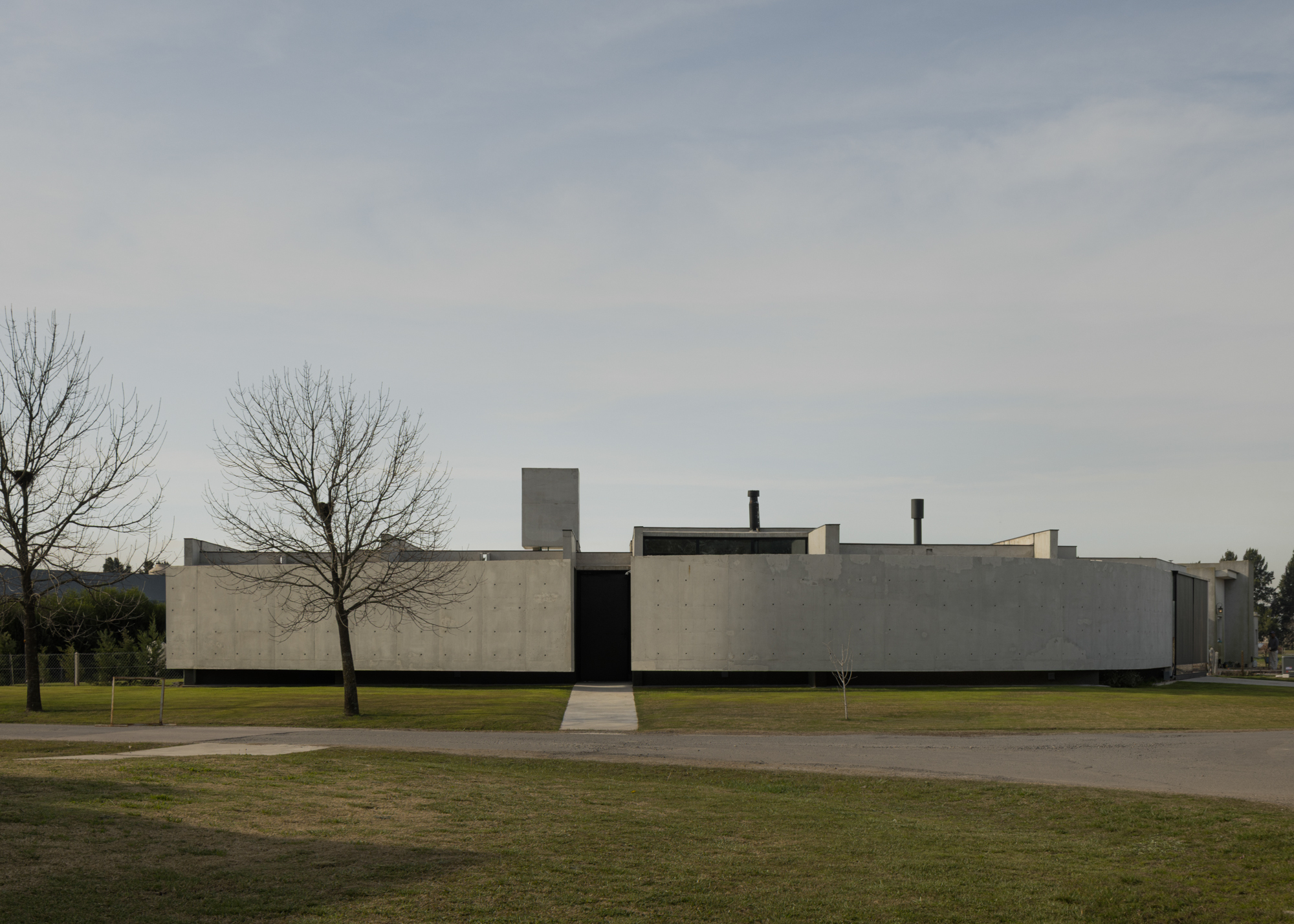 Long horizontal concrete facade with central entry flanked by bare trees on a lawn