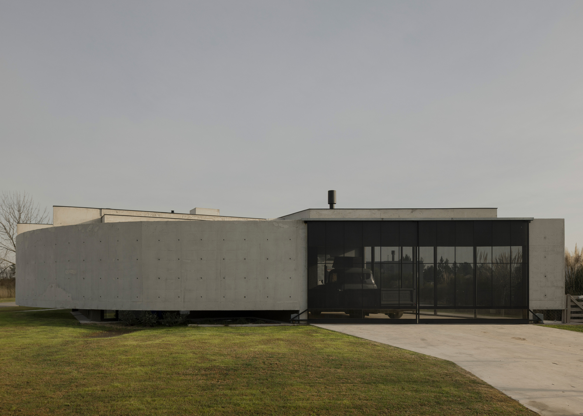 Entrance facade with full-height glazing set between projecting concrete volumes under grey skies