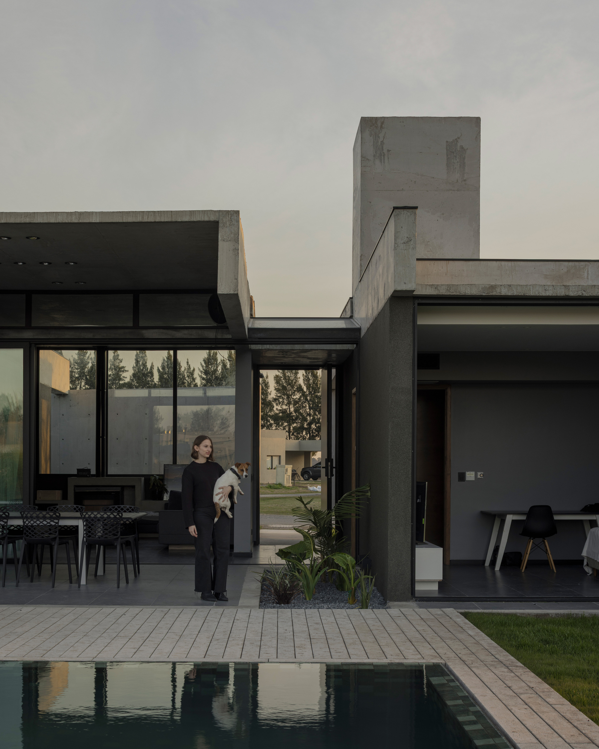 Courtyard with swimming pool and concrete tower viewed past a woman standing among potted plants
