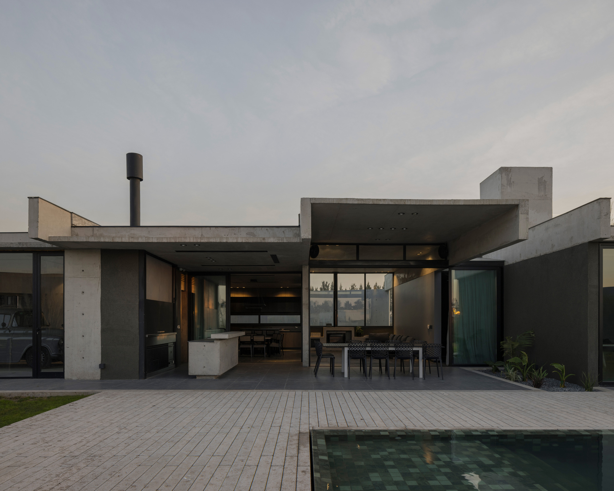 Covered outdoor terrace with exposed concrete beams overlooking a paved deck and pool at dusk